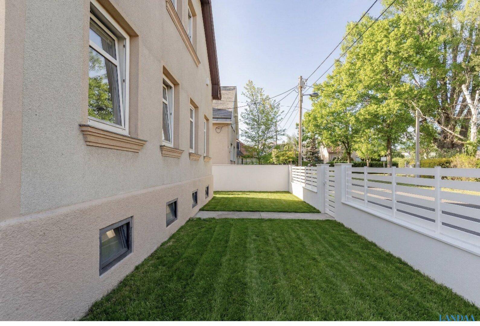 Seitlicher Gartenbereich mit gepflegtem Rasen und moderner Zaunanlage entlang des Hauses.