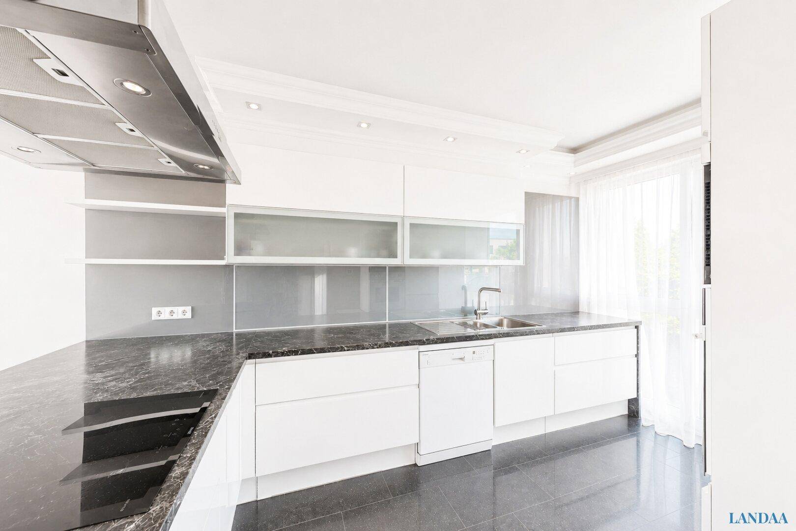 Moderne Küche mit weißen Schränken, dunklen Arbeitsplatten und integrierten Geräten.