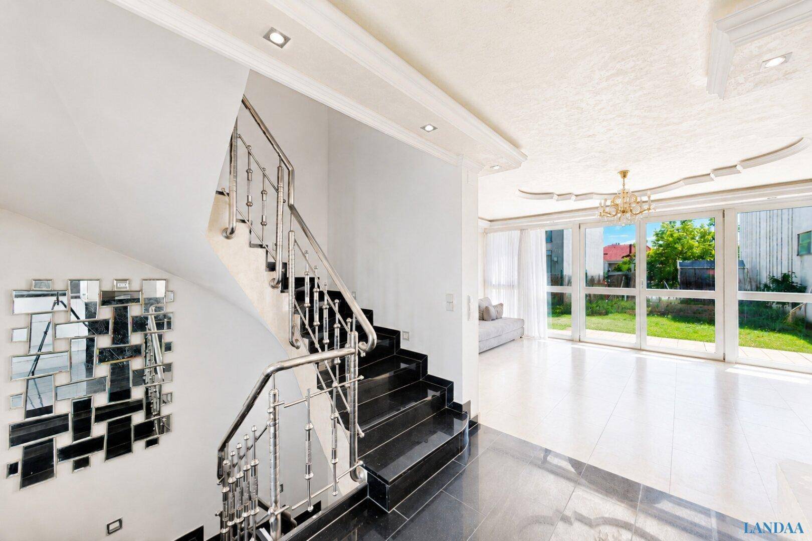 Eleganter Flur mit moderner Treppe und Blick durch große Fenster in den Garten.