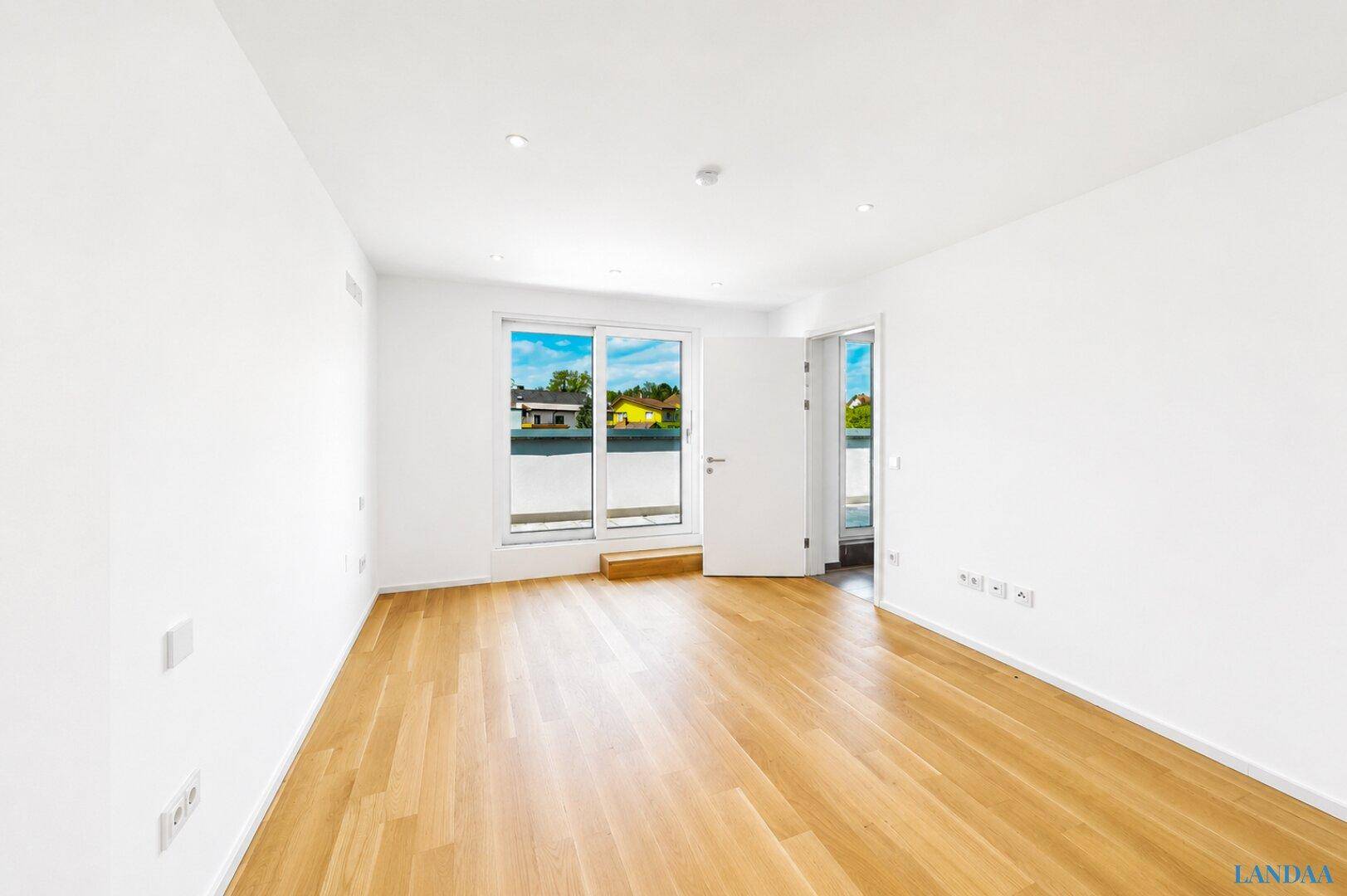 Heller Raum mit Holzboden und Zugang zu einem Balkon, bietet vielseitige Nutzungsmöglichkeiten.