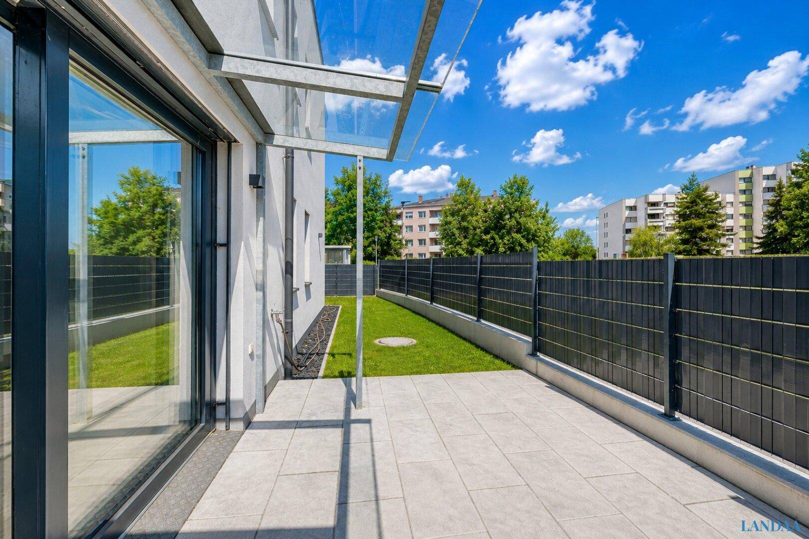 Terrasse mit Zugang zum Garten und Blick auf die umliegenden Gebäude und Grünflächen.