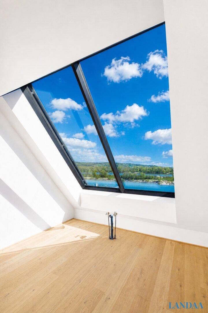 Geräumiger, heller Raum mit schrägen Wänden, Holzboden und einem großen Dachfenster mit Seeblick.