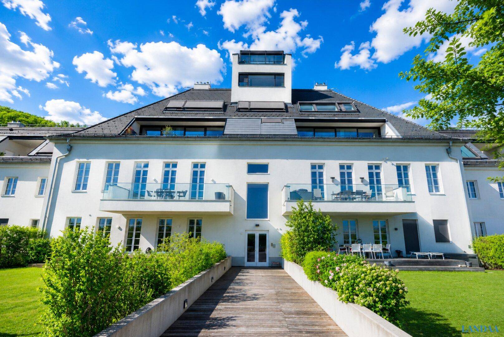 Elegante weiße Fassade eines modernen Gebäudes mit mehreren Balkonen und grüner Umgebung.