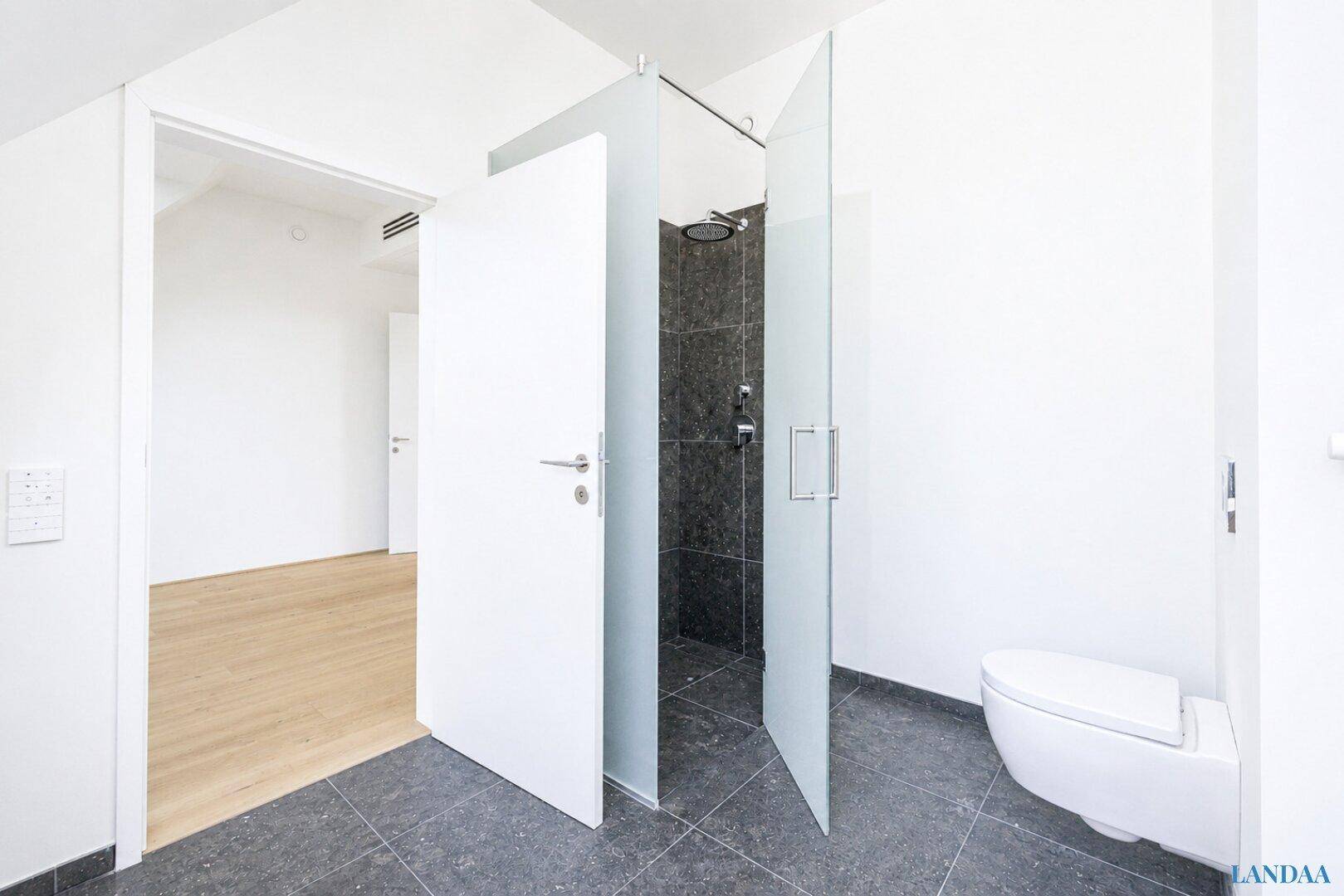 Modernes Badezimmer mit dunklen Fliesen, begehbarer Dusche und wandmontierter Toilette.
