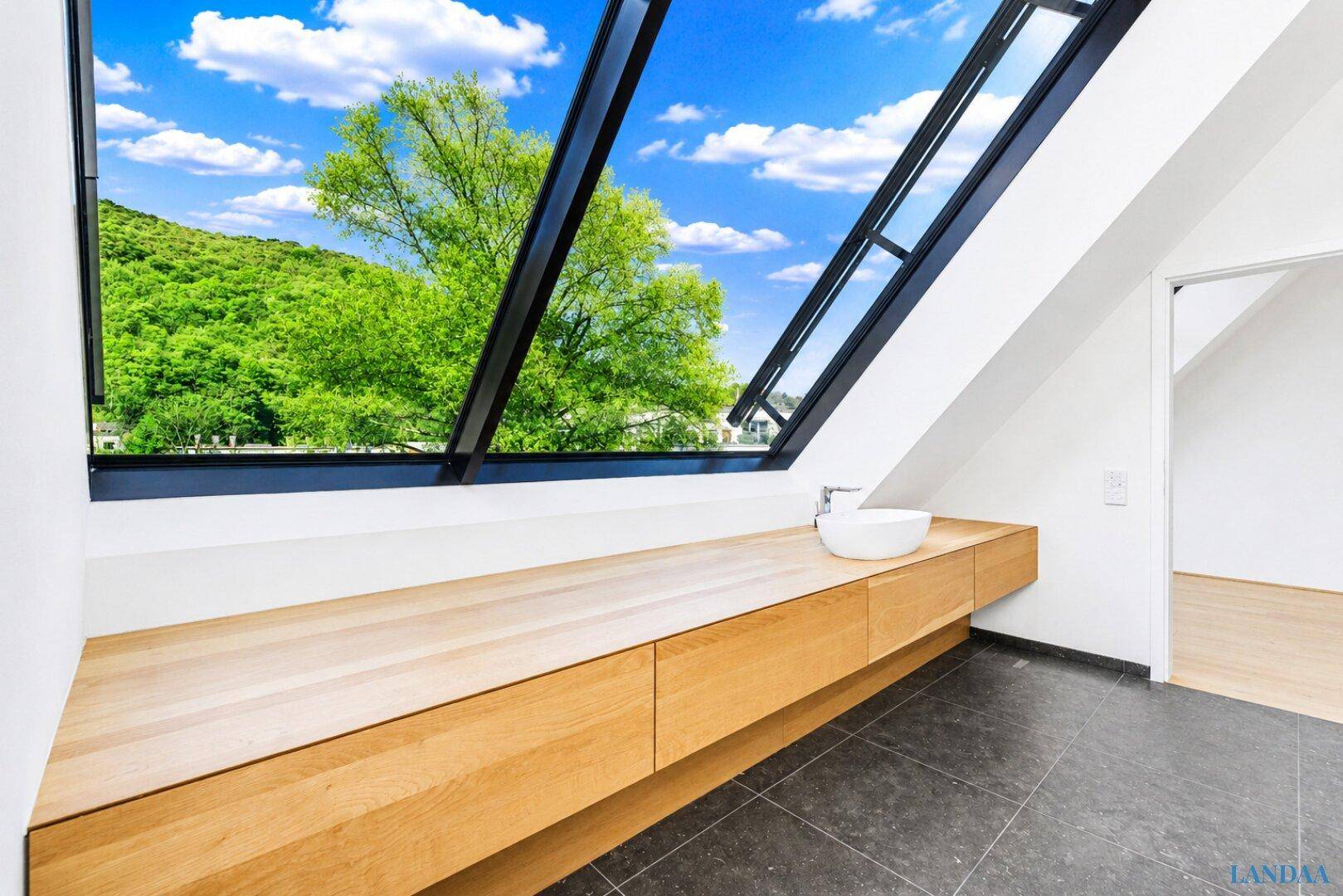 Modernes Badezimmer mit Holztresen, Aufsatzwaschbecken und großem Fenster mit Blick ins Grüne.