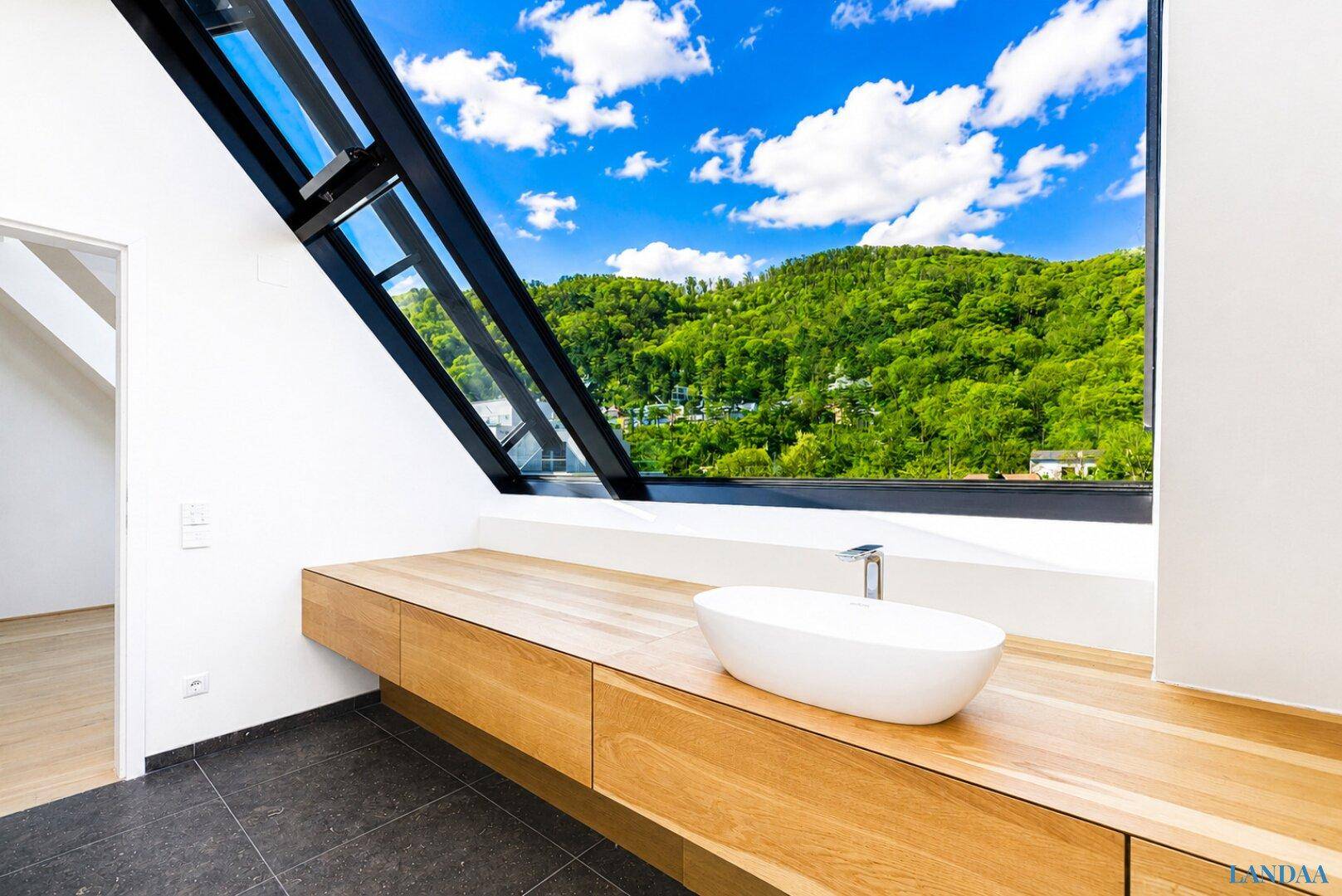 Modernes Badezimmer mit Holztresen, Aufsatzwaschbecken und großem Fenster mit Blick ins Grüne.
