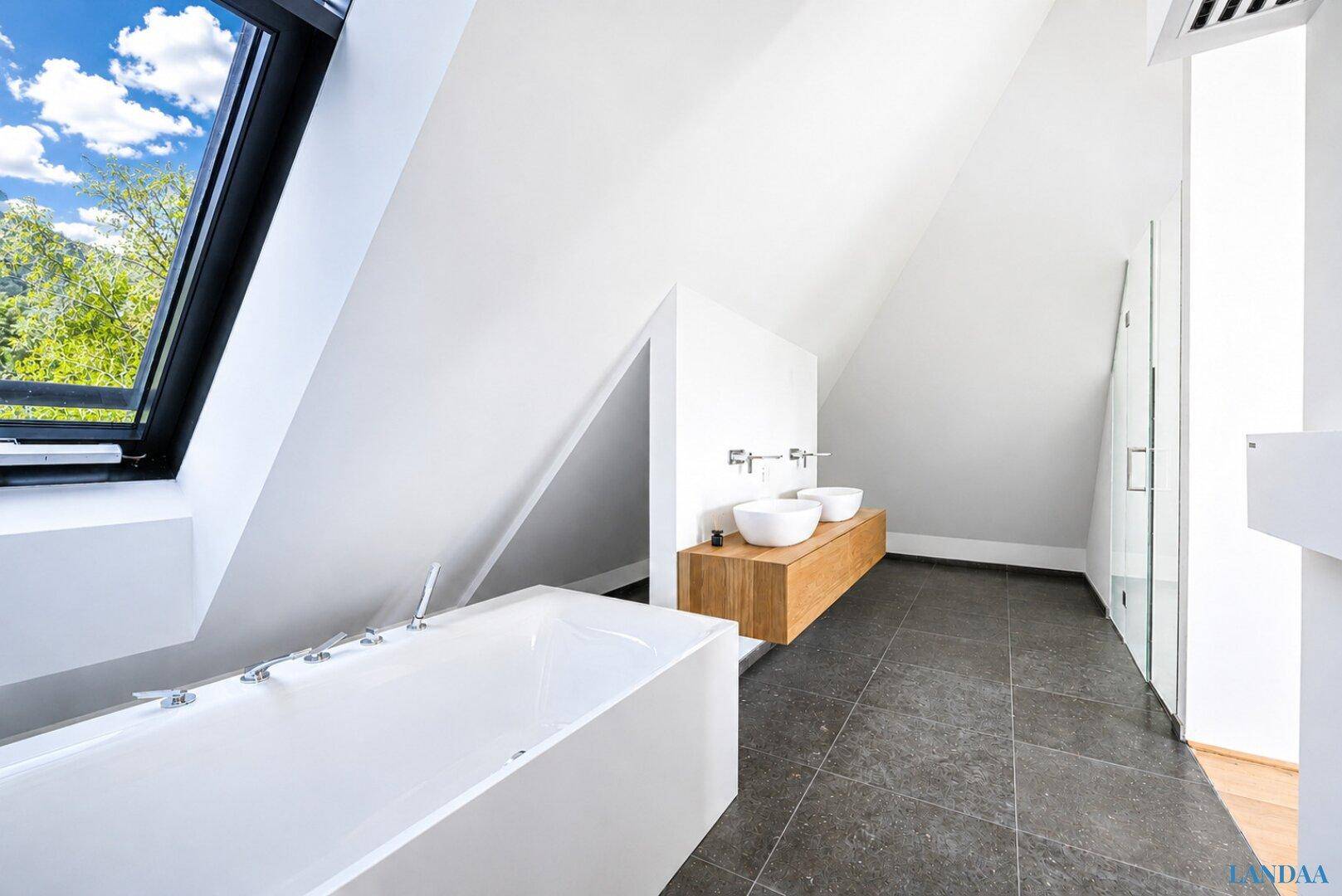 Luxuriöses Badezimmer mit freistehender Badewanne, Doppelwaschbecken und großen Fenstern mit Blick ins Grüne.
