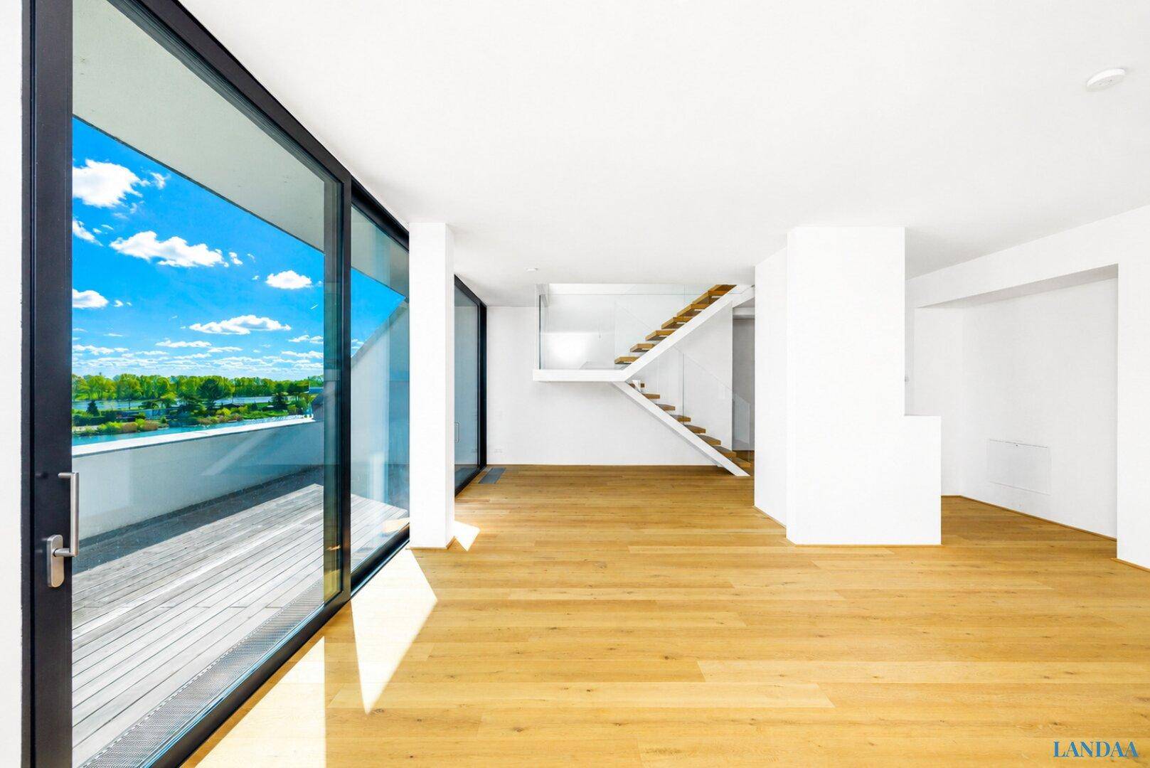 Offener, heller Wohnbereich mit Holzboden, moderner Treppe und Zugang zu einer Terrasse mit Seeblick.