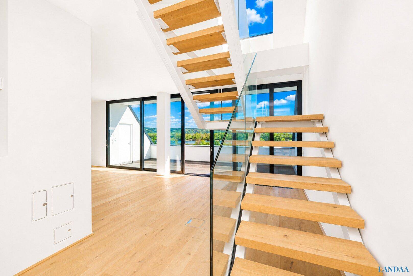 Heller, offener Wohnbereich mit moderner Holztreppe, Glasgeländer und weitem Ausblick.