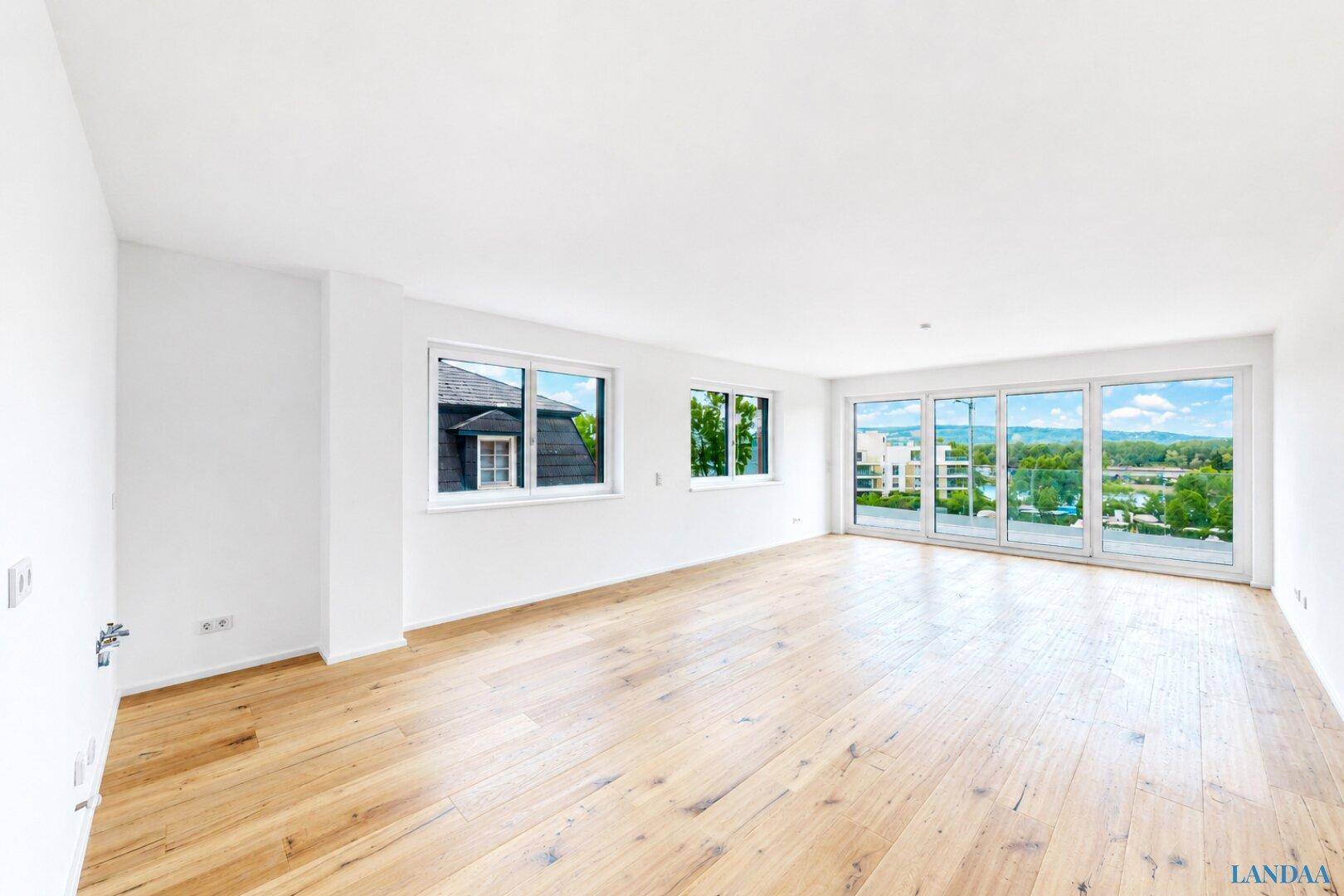Helles, leeres Wohnzimmer mit Holzboden und großen Fenstern mit weitem Ausblick.