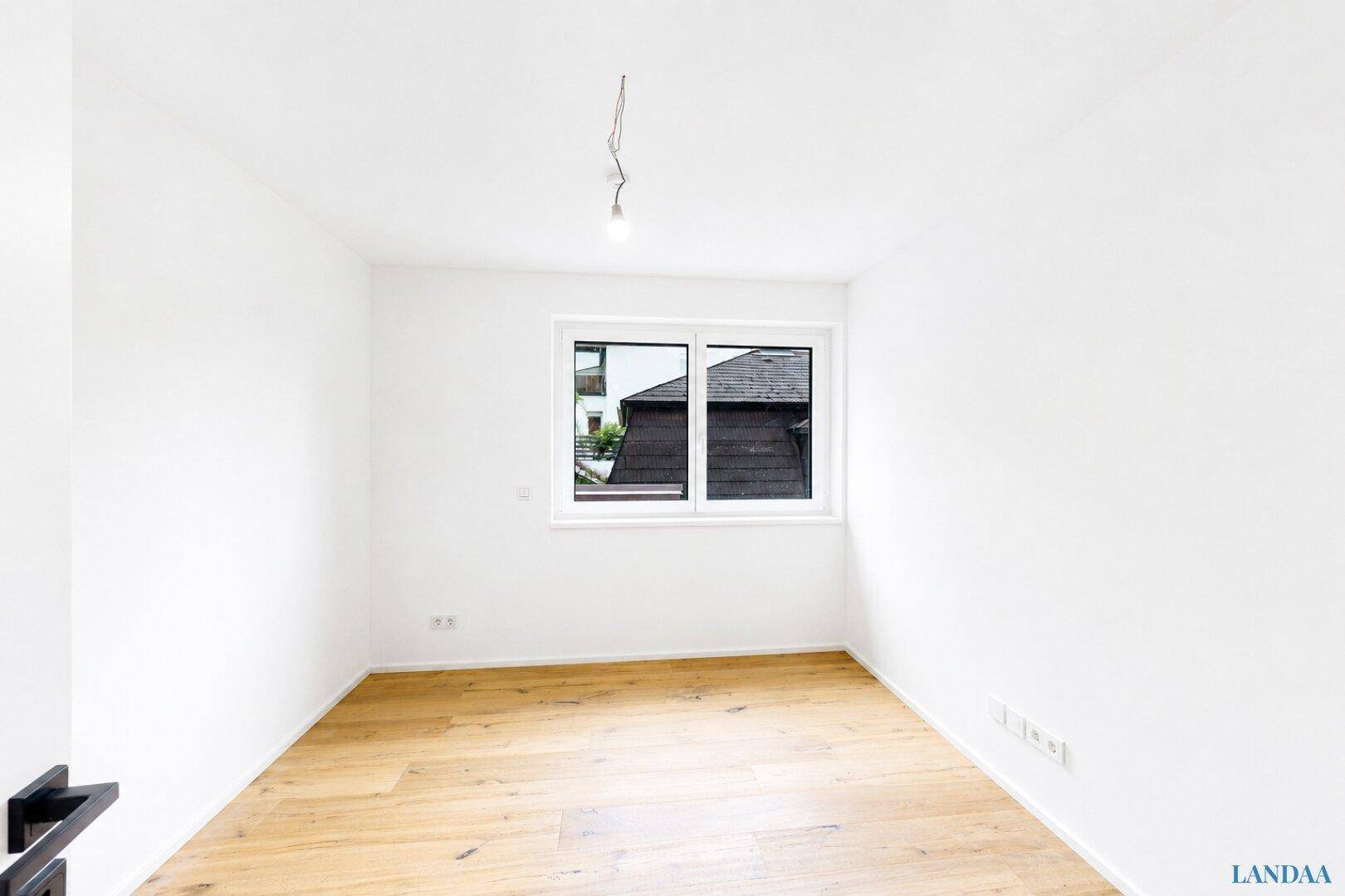 Leeres Zimmer mit Holzboden und Fenster, bereit zur individuellen Gestaltung.