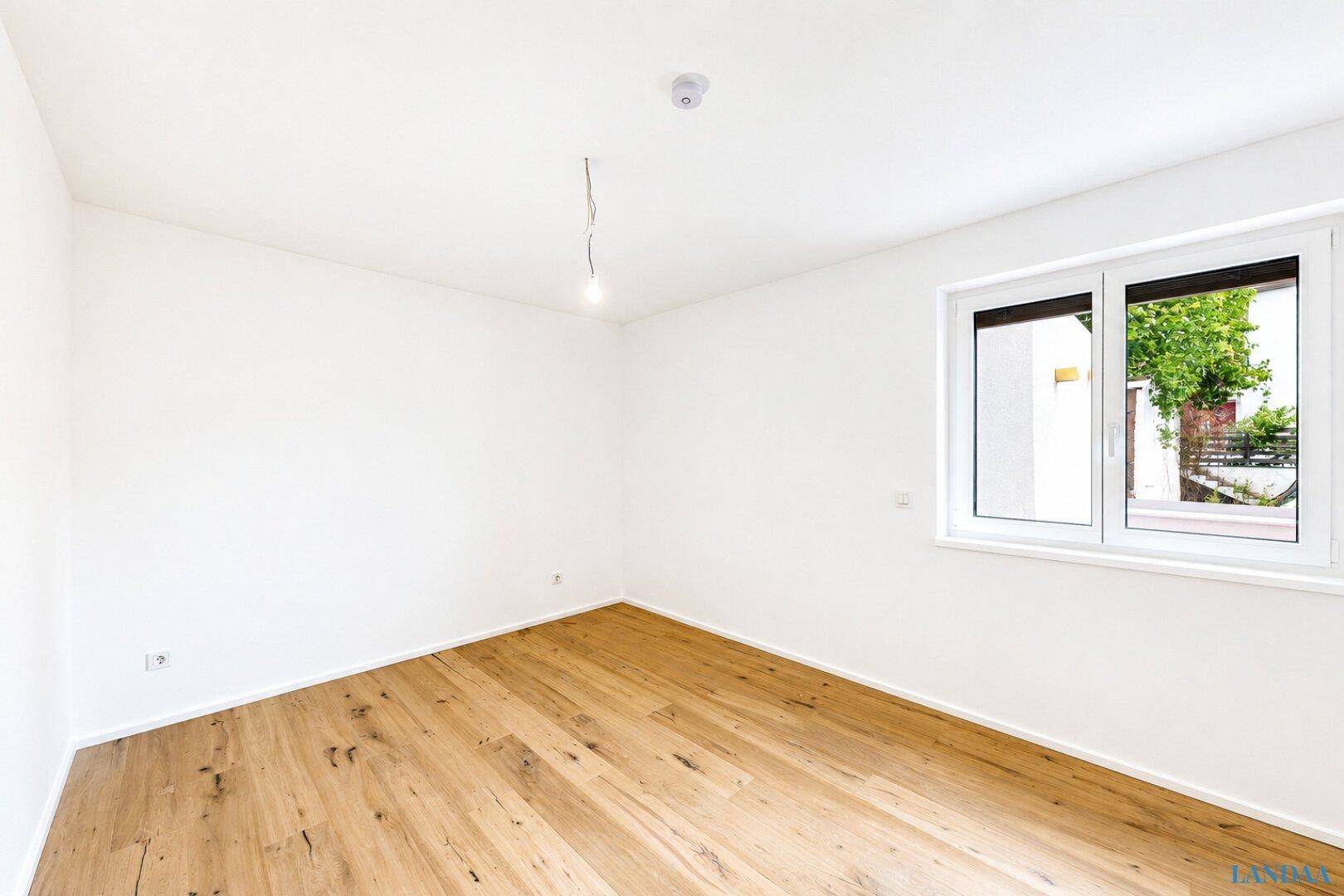 Helles, unmöbliertes Zimmer mit Holzboden und Fenster, ideal für Schlaf- oder Arbeitsbereich.