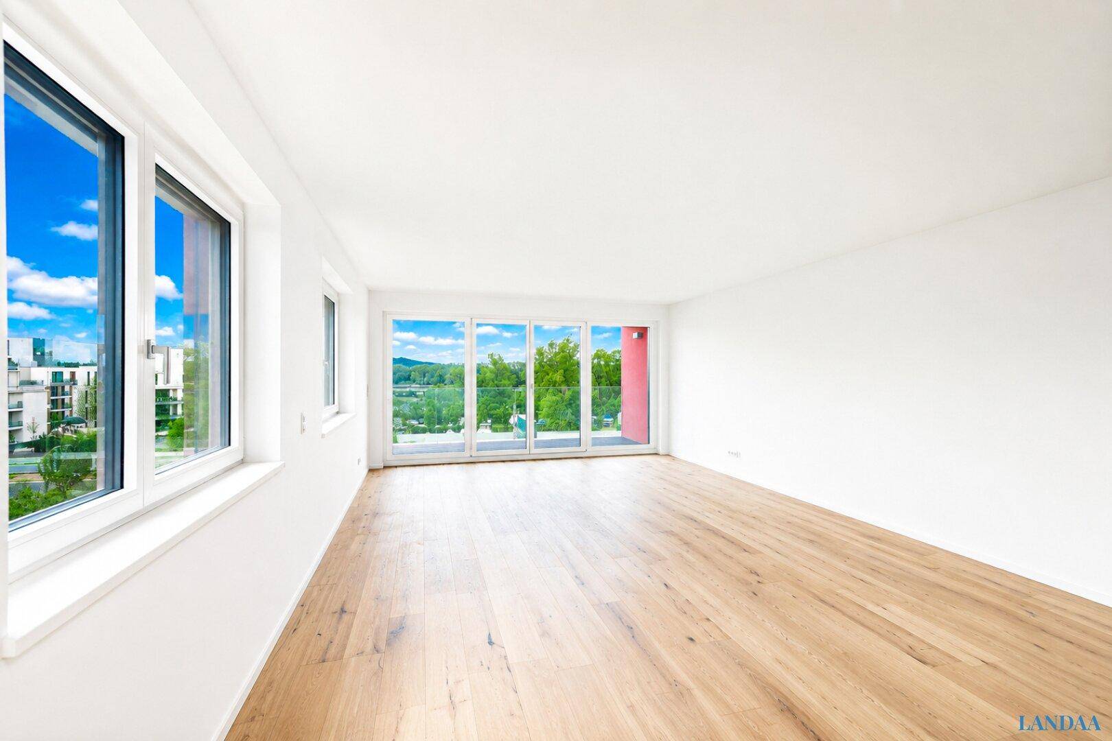 Geräumiges, helles Wohnzimmer mit Holzboden und großen Fenstern, die viel Licht hereinlassen.
