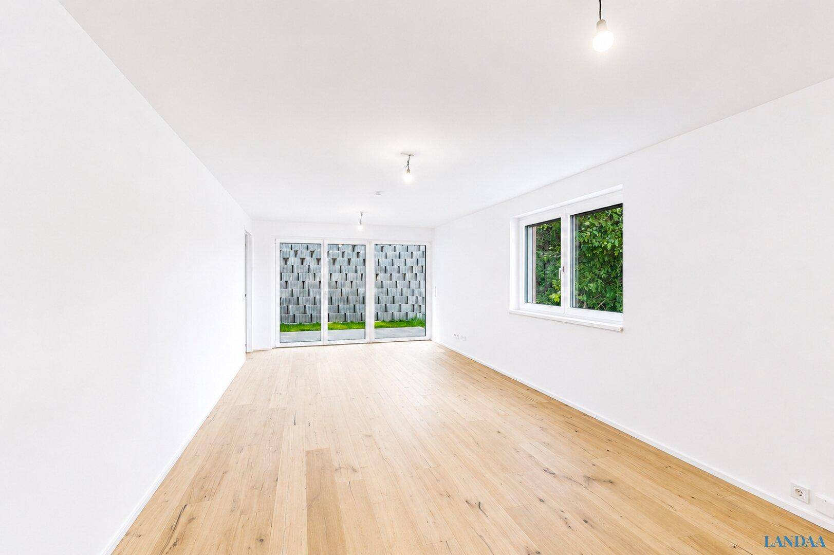 Geräumiger, heller Raum mit Holzboden und großen Fenstern, die viel Tageslicht hereinlassen.