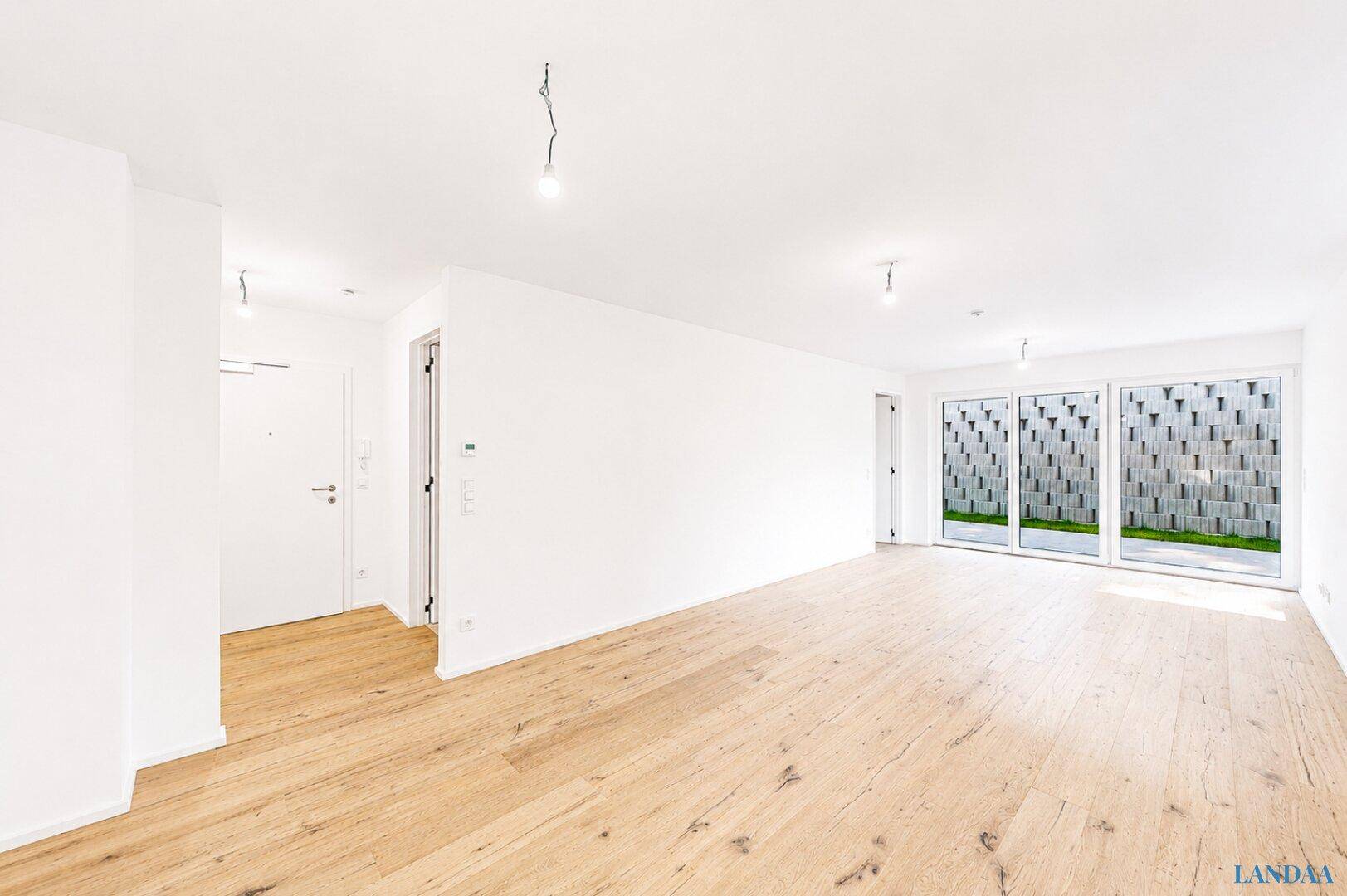 Heller Eingangsbereich mit Holzboden, der in einen offenen Wohnbereich mit Terrassenzugang übergeht.