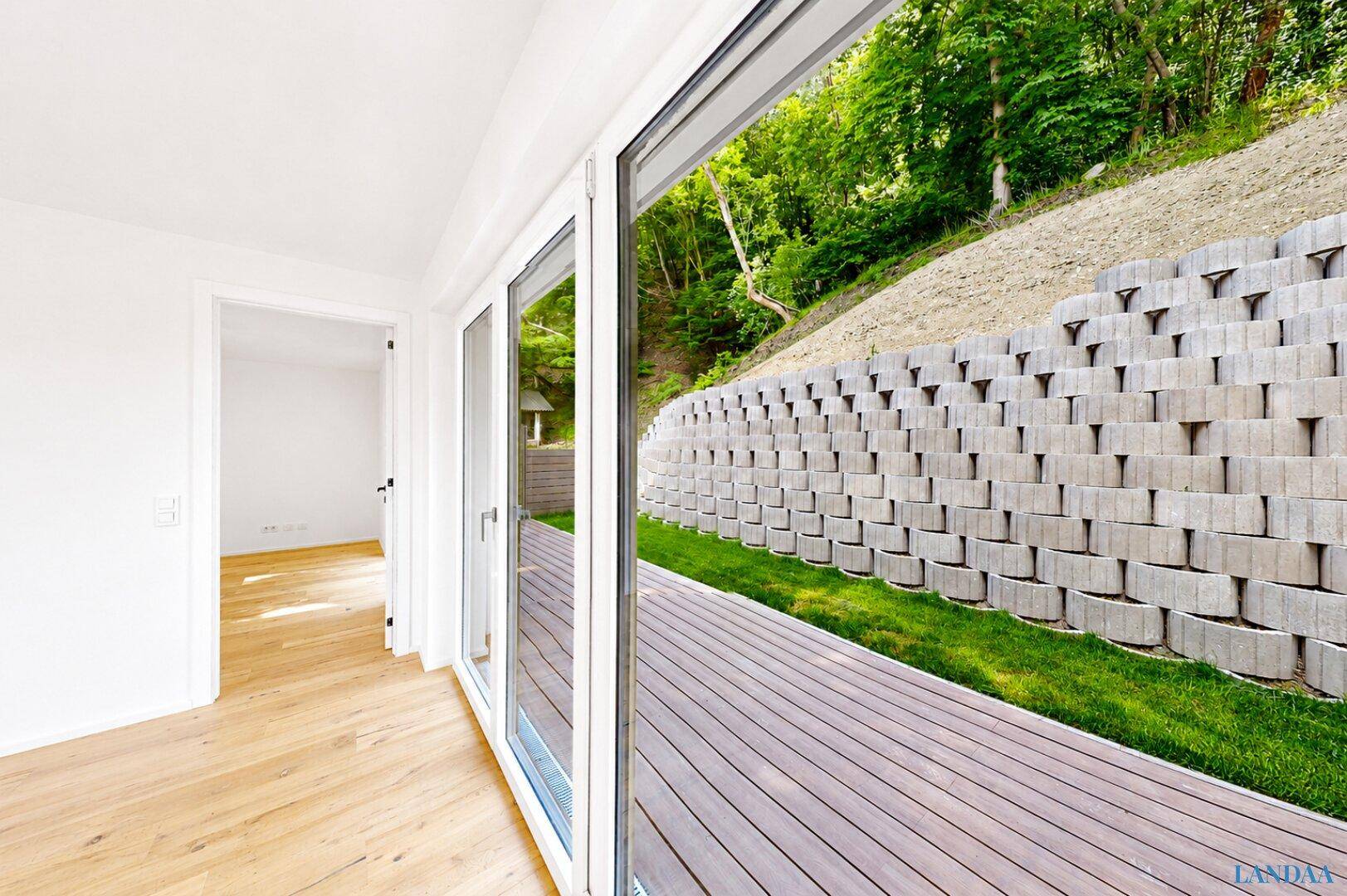 Holzterrasse mit Blick auf eine begrünte Böschung und viel Grün, ideal zum Entspannen.