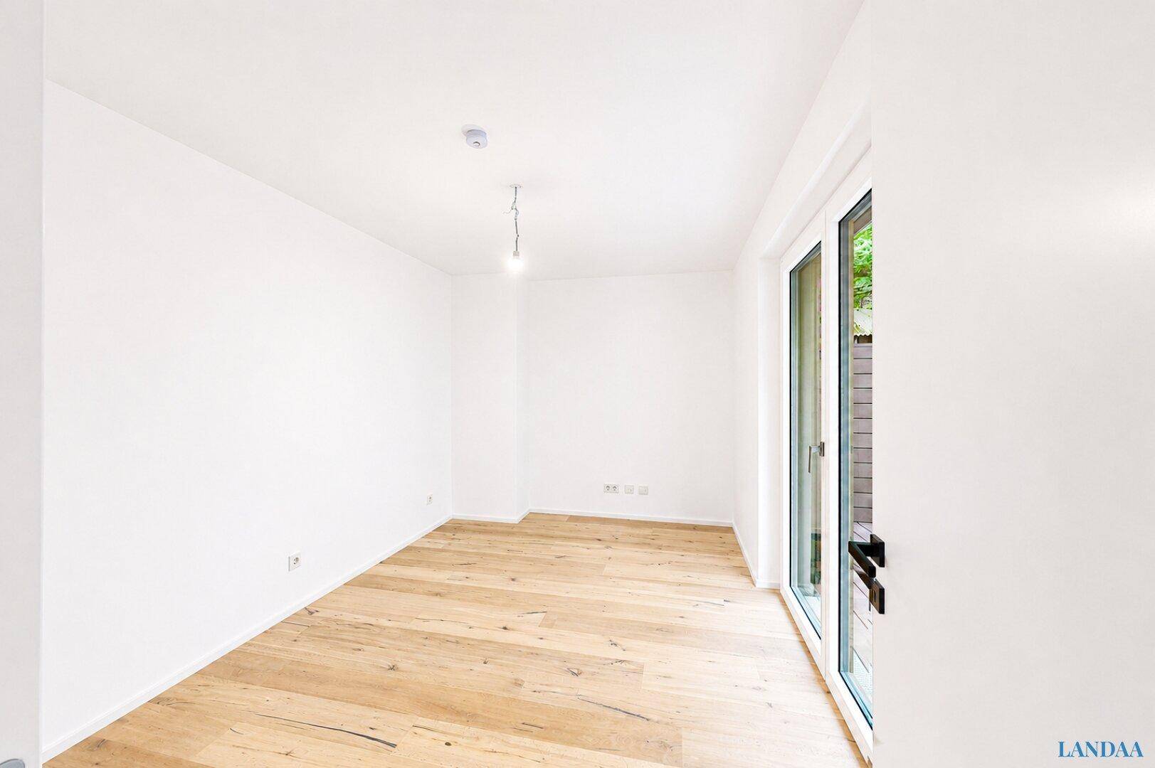 Heller, unmöblierter Raum mit Holzboden und großen Fenstern, die viel Tageslicht hereinlassen.