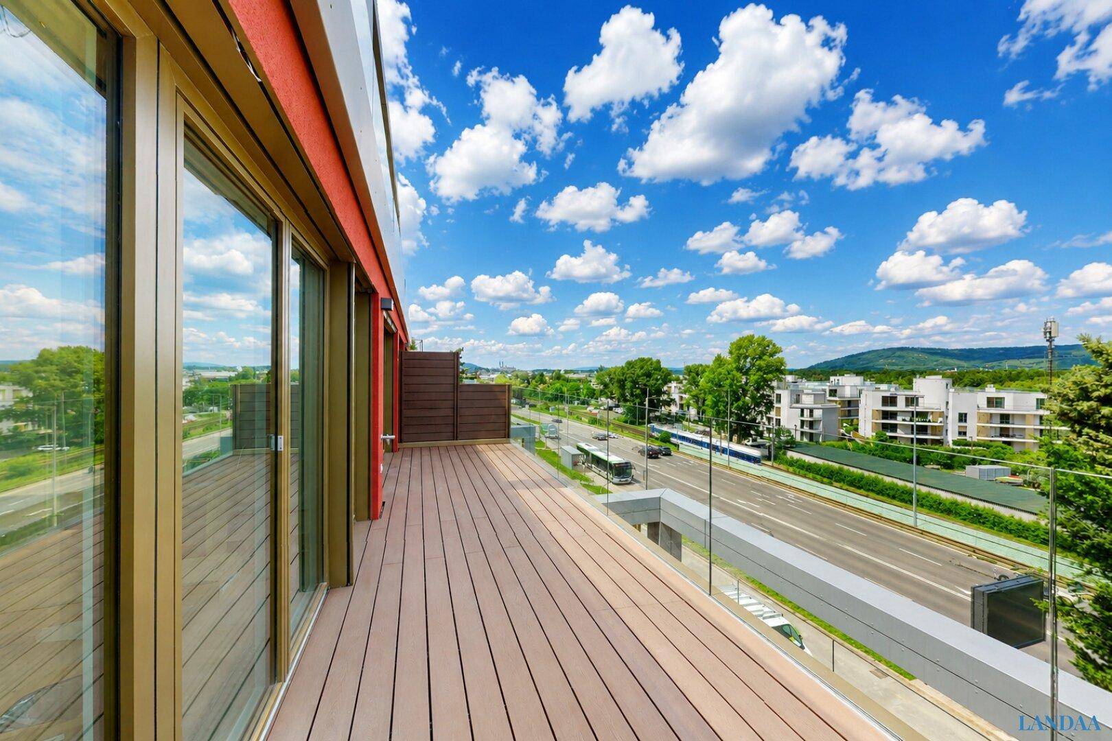 Geräumige Terrasse mit Holzbelag und Glasbrüstung, bietet weiten Blick auf die Umgebung.
