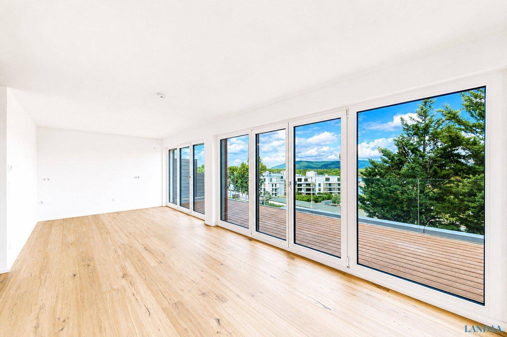 Heller Raum mit Holzboden und großen Fensterfronten, die einen weiten Blick ins Grüne bieten.