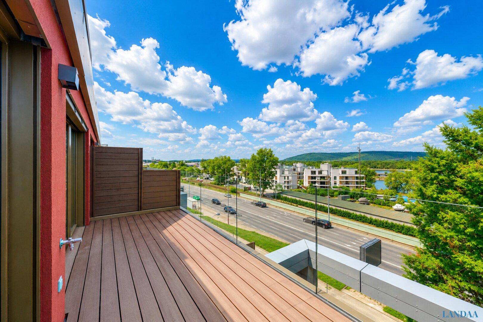 Große Holzterrasse mit Glasbrüstung und weitem Blick auf die Straße und die umliegende Landschaft.