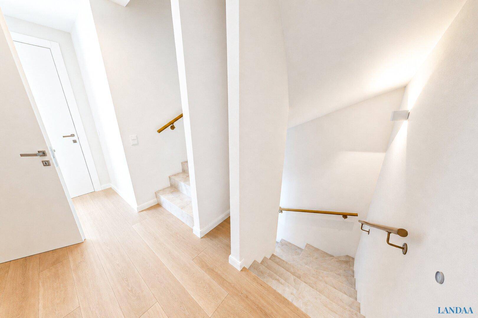 Heller Flur mit eleganter Treppe und Holzboden, der die verschiedenen Ebenen verbindet.