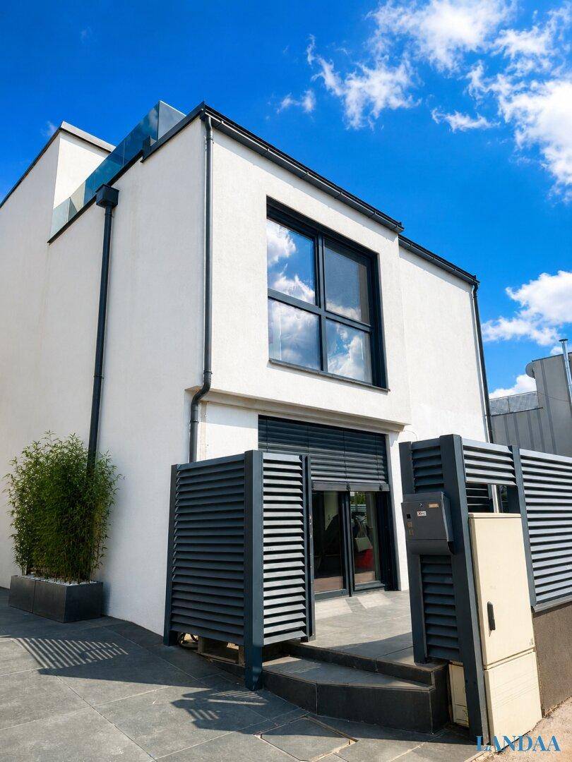 Seitenansicht der modernen weißen Villa mit schwarzen Fensterläden und minimalistischer Bepflanzung.