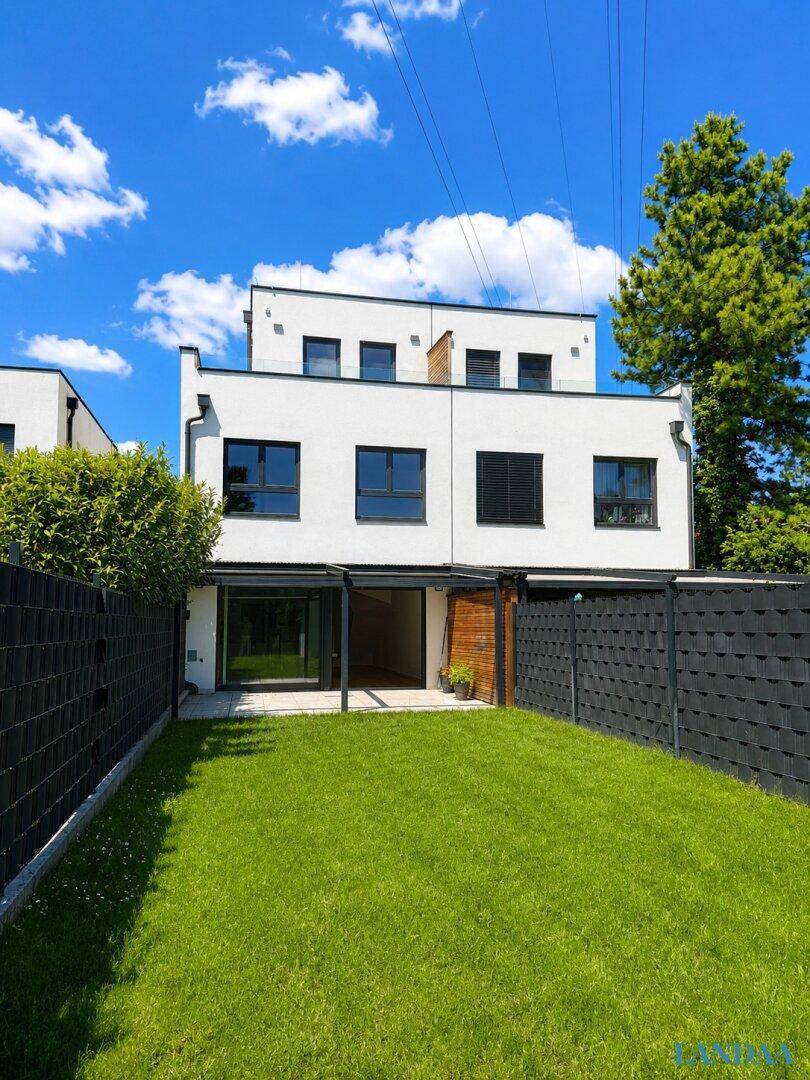 Gepflegter Garten hinter dem modernen Reihenhaus mit Rasenfläche und großer Glasfront.