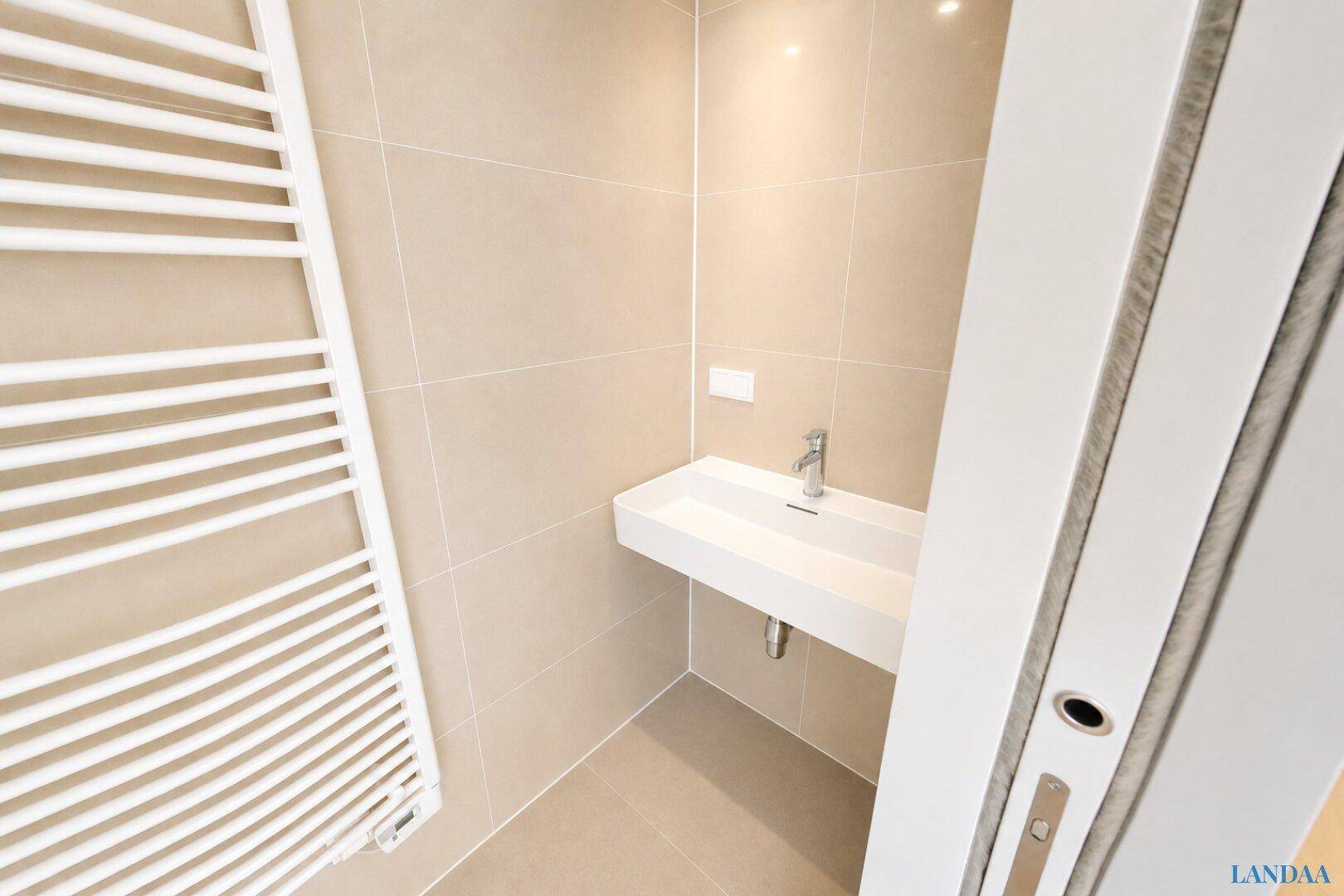 Modernes WC mit beigefarbenen Fliesen, einem Waschbecken und einem beheizten Handtuchhalter.