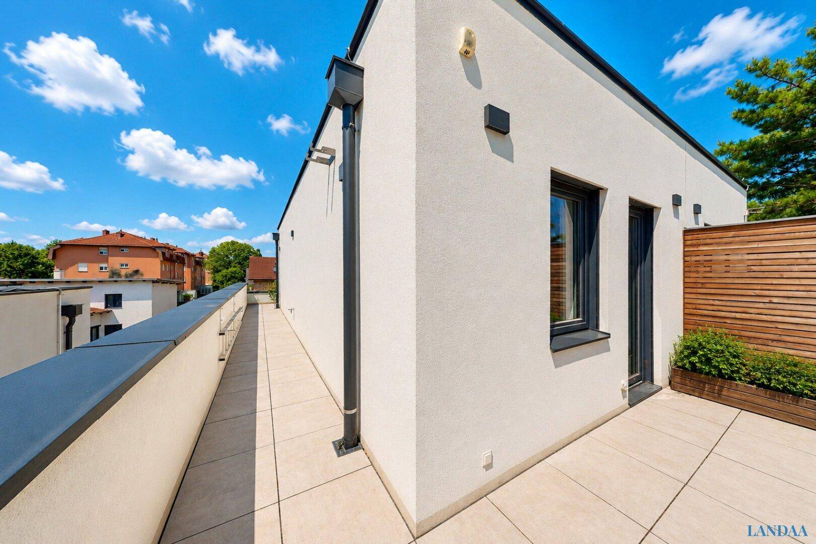 Geräumige Dachterrasse mit weißer Fassade und Holzelementen für Privatsphäre.