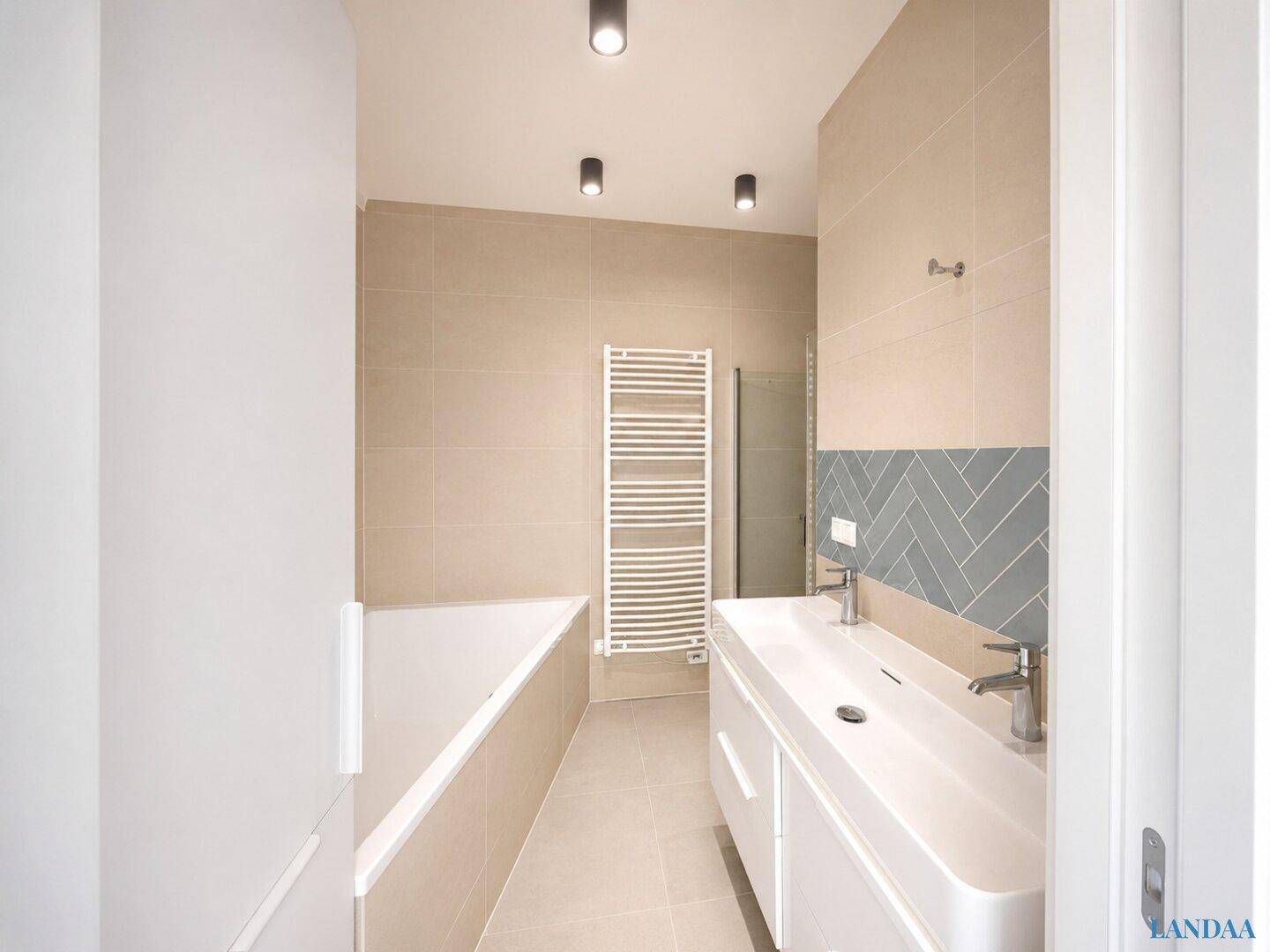 Modernes Badezimmer mit Doppelwaschbecken, Badewanne und beigefarbenen Fliesen.