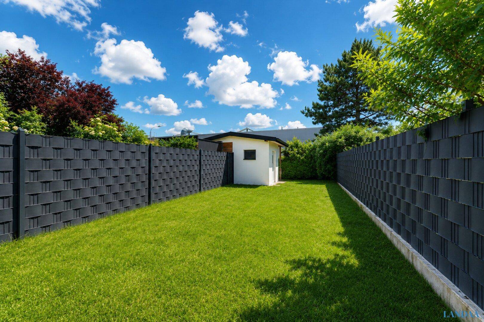 Sonniger Garten mit Rasenfläche, Sichtschutzzaun und einem kleinen Gartenhaus.