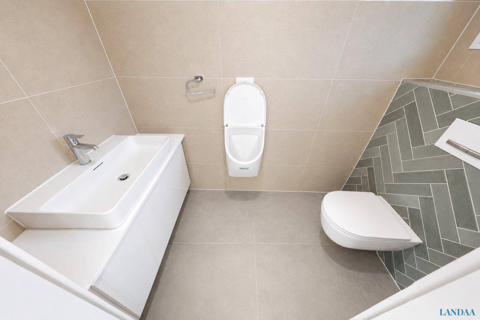 Modernes Badezimmer mit Wand-WC, Urinal und elegantem Waschbecken mit Unterschrank.