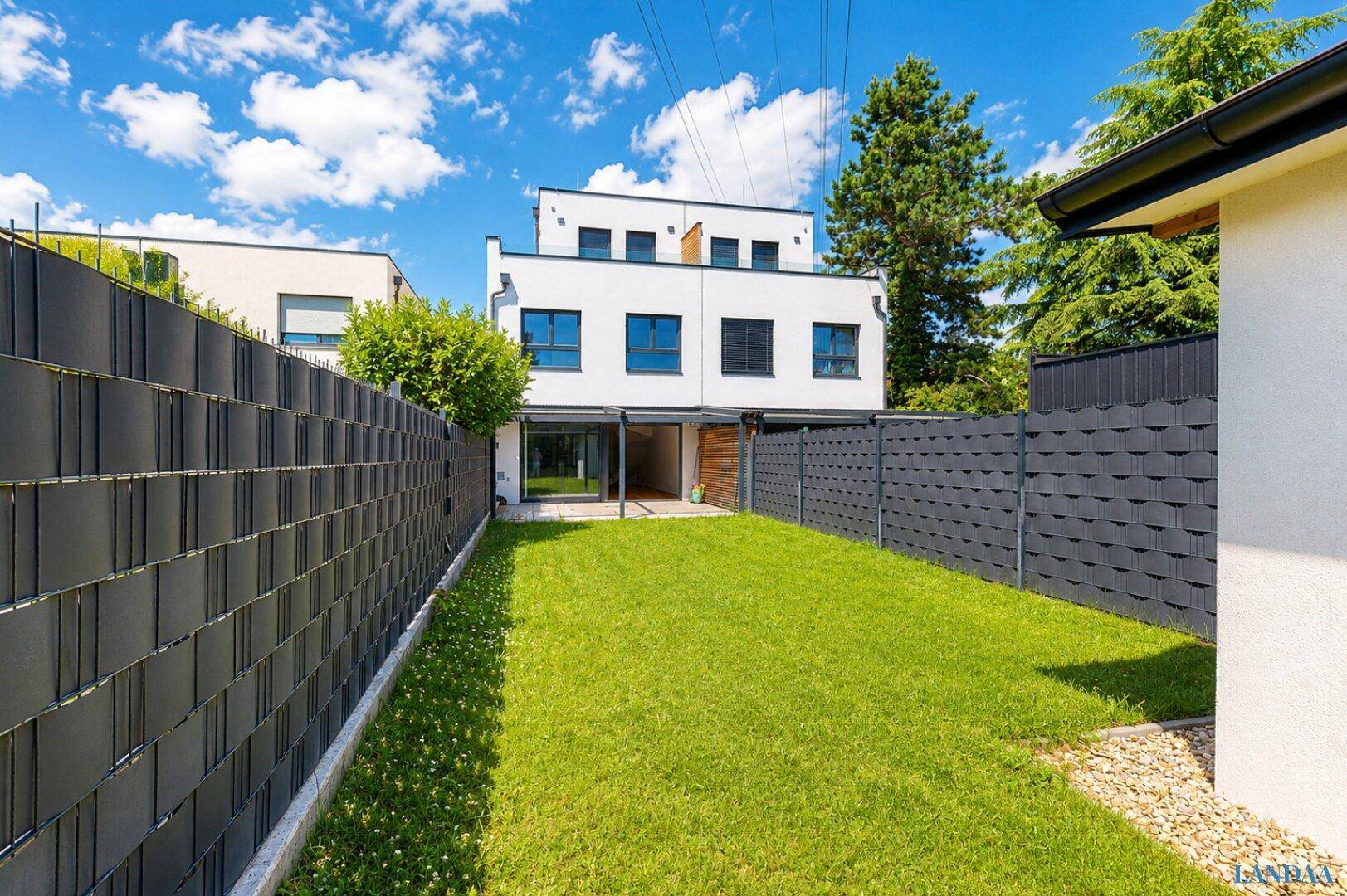 Gepflegter Garten mit Rasenfläche und moderner Zaunanlage hinter dem Wohngebäude.