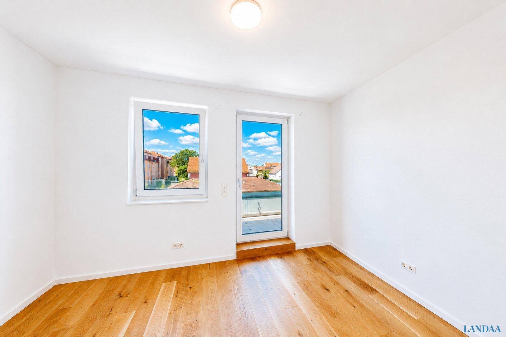Helles Zimmer mit Holzboden und Zugang zu einem Balkon oder einer Terrasse.