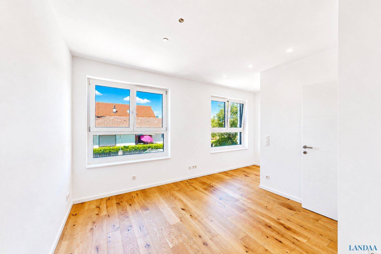 Geräumiges Zimmer mit Holzboden und zwei großen Fenstern für viel Tageslicht.