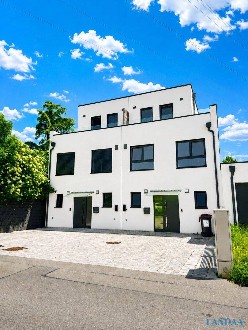 Moderne Doppelhaushälfte mit weißer Fassade, dunklen Fenstern und klarem Himmel.