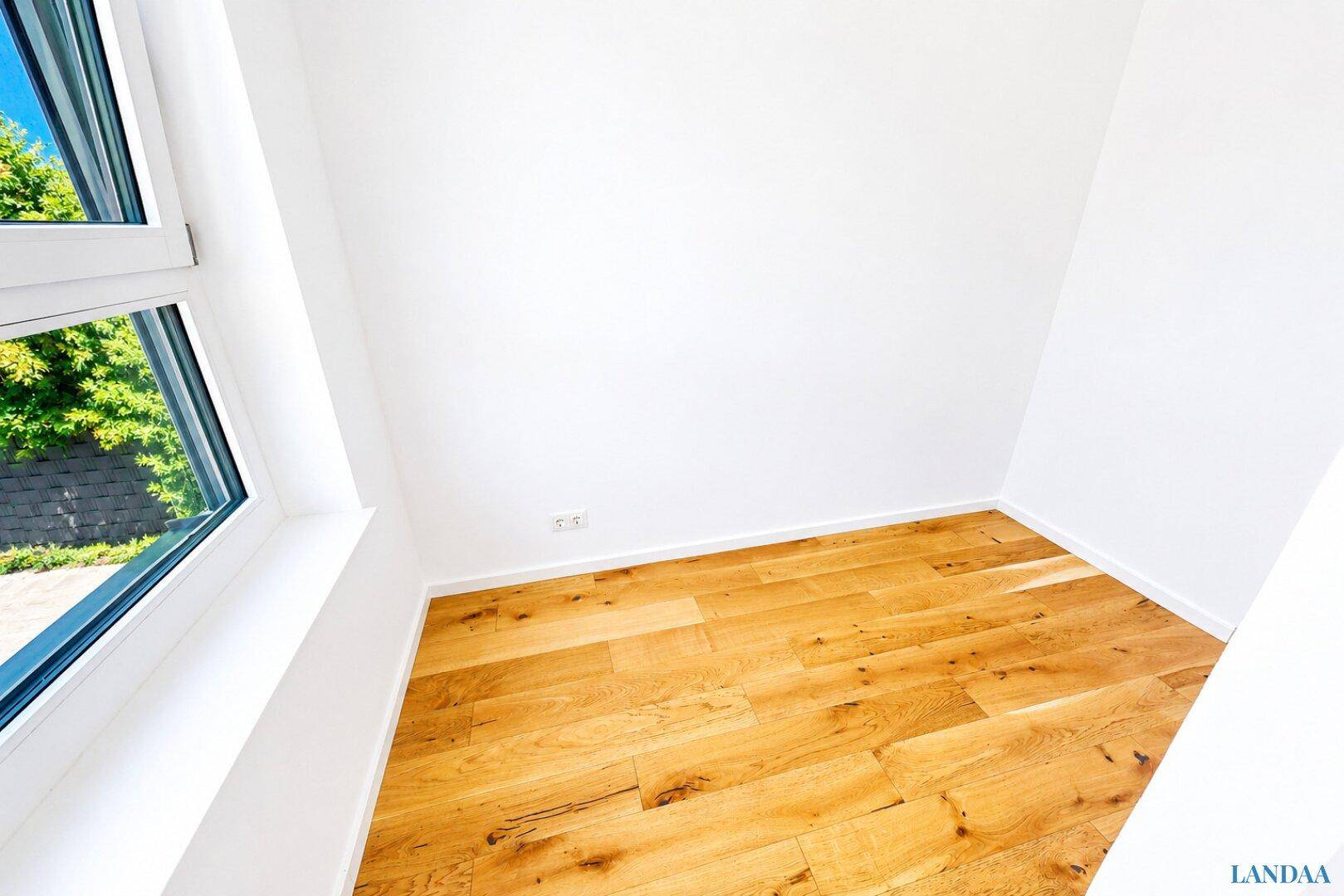 Helles Zimmer mit schönem Holzboden und einem Fenster mit Blick ins Grüne.