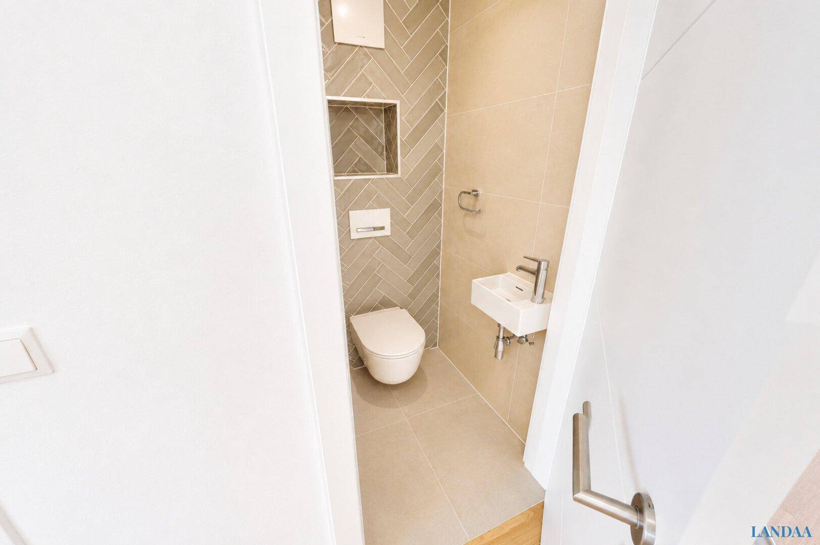 Kompaktes Gäste-WC mit modernem Wand-WC und kleinem Waschbecken, elegant gefliest.