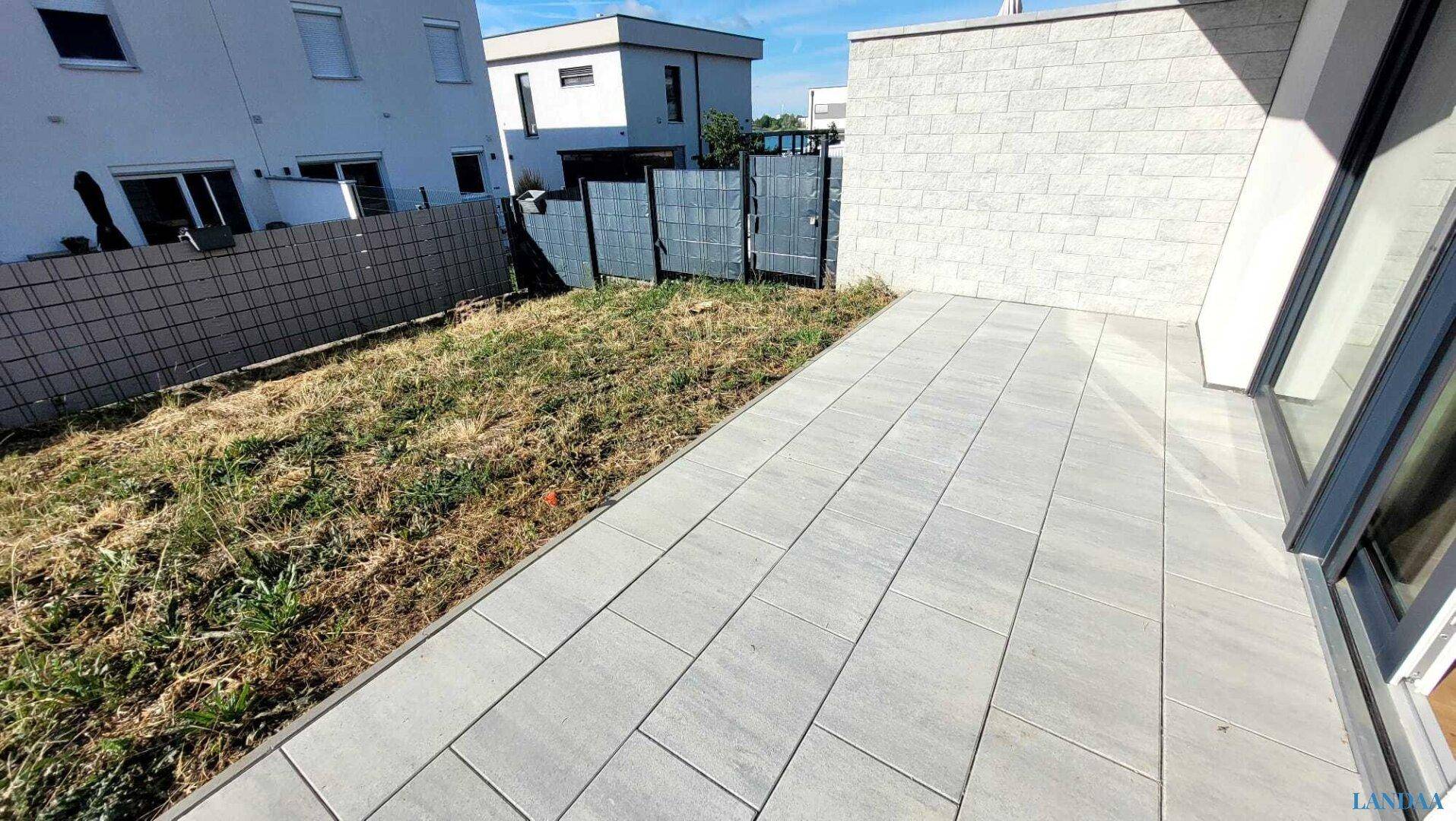 Terrasse mit Pflastersteinen und angrenzendem, noch ungestaltetem Gartenbereich.