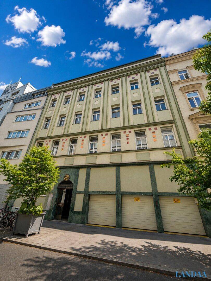 Historisches Gebäude mit grüner Fassade, vielen Fenstern und Garagentoren im Erdgeschoss.