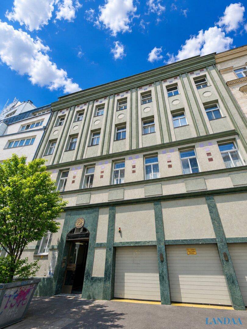 Historisches Gebäude mit grüner Fassade, vielen Fenstern und Garagentoren im Erdgeschoss.