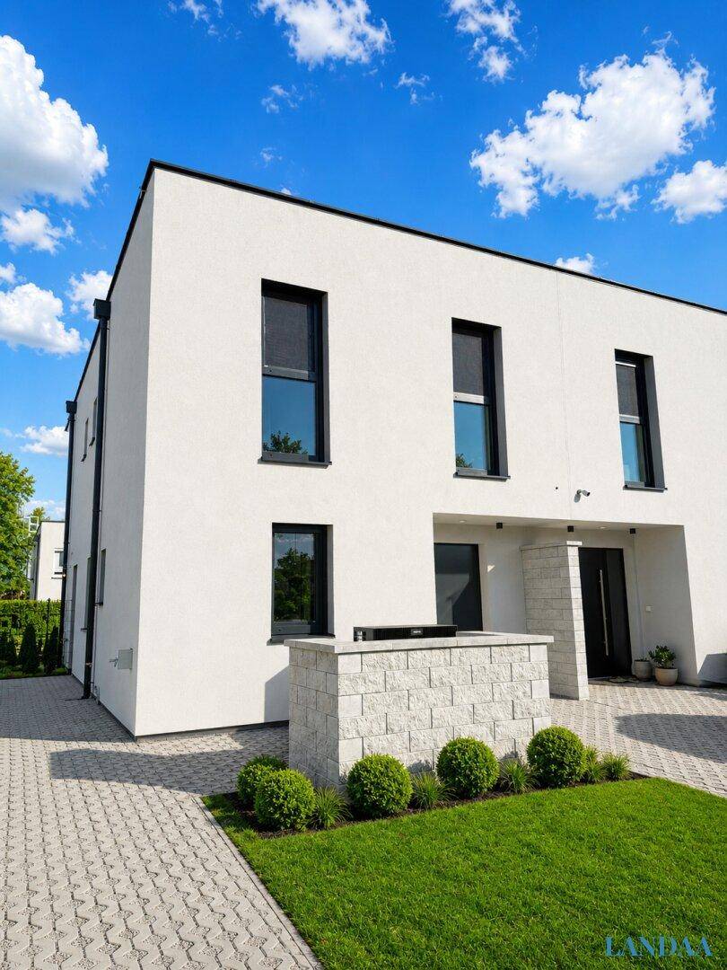 Moderne Hausfassade in Weiß mit dunklen Fensterrahmen und gepflegtem Vorgarten.
