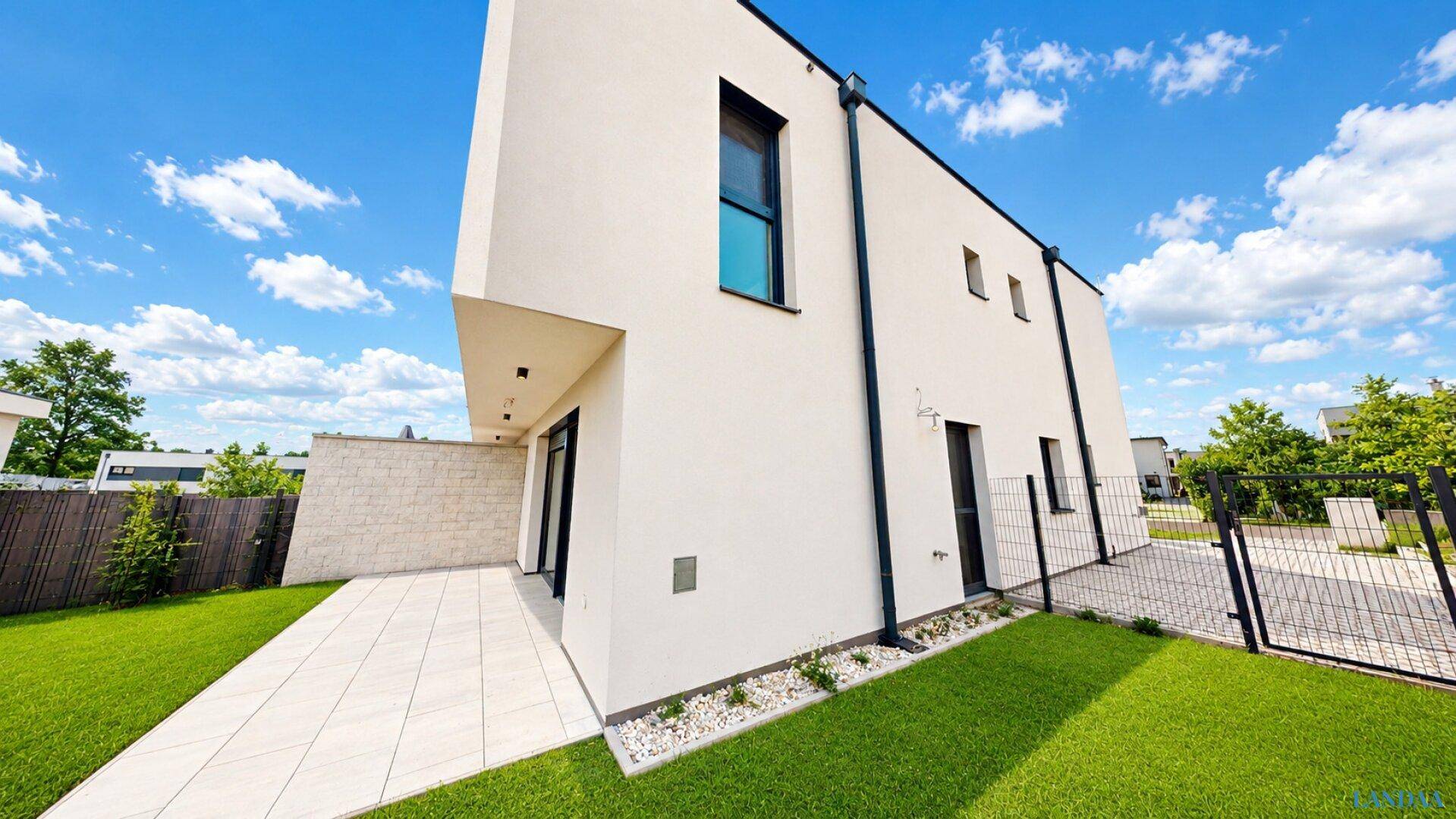 Seitenansicht des modernen Hauses mit Terrasse und gepflegtem Rasenbereich.