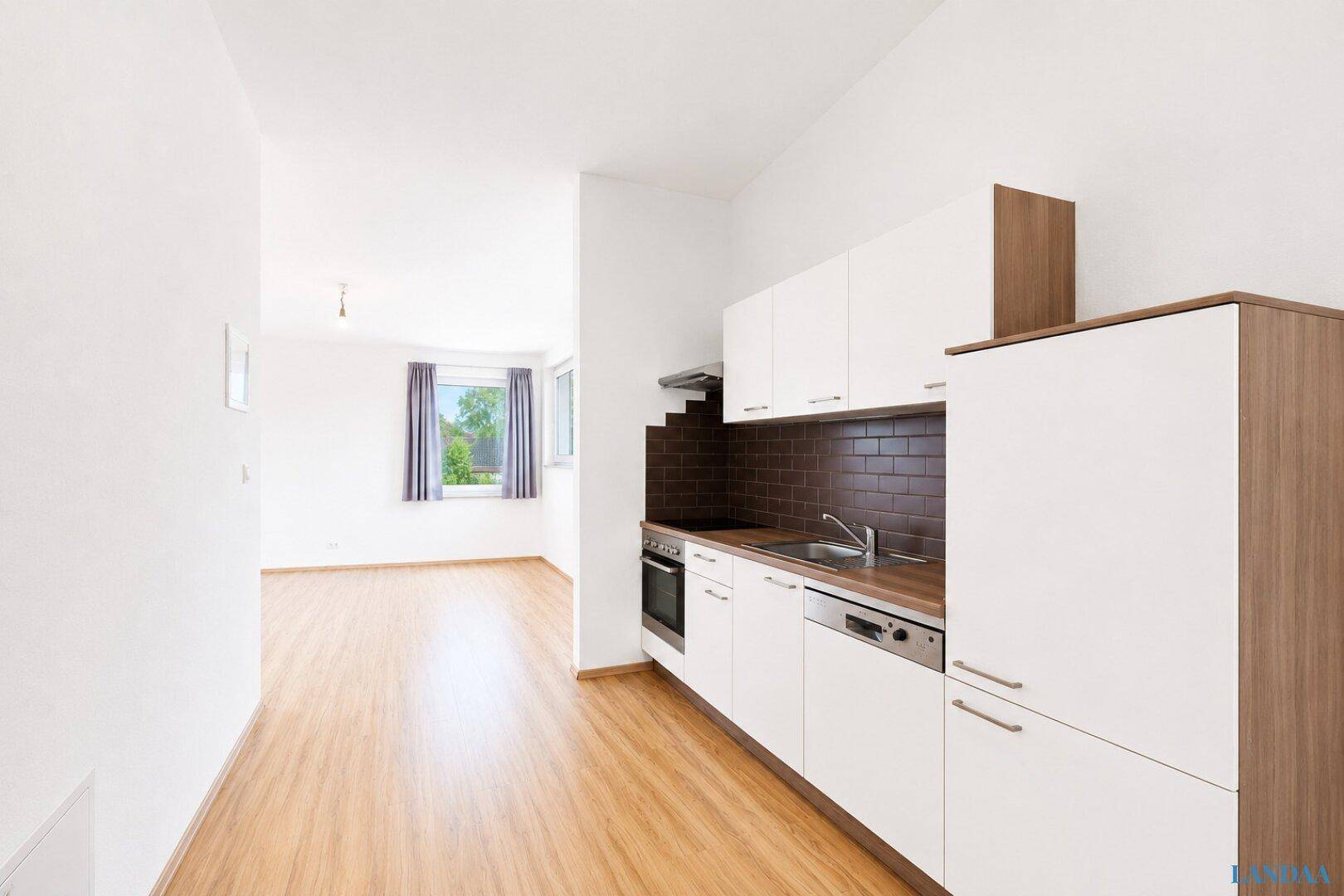 Moderne Küchenzeile in einem hellen, offenen Wohnbereich mit Holzboden und Blick ins Grüne.