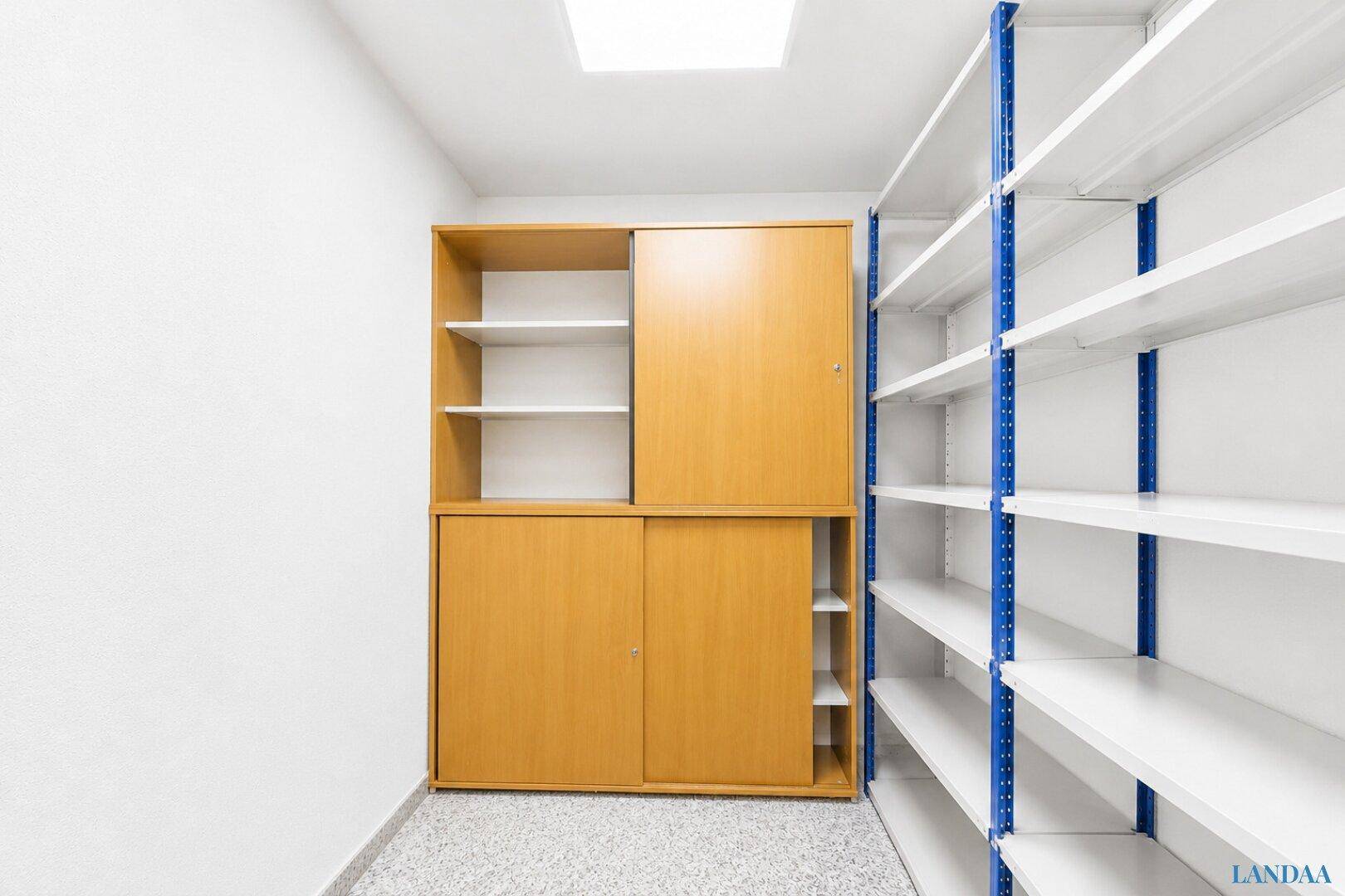 Ordentlicher Abstellraum mit weißen Wänden, hellem Terrazzoboden, Holzschrank und Metallregalen für Lagerung.