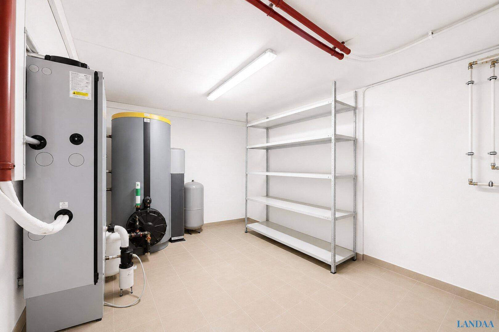 Technischer Raum mit großen Wassertanks, sichtbaren Rohren und Metallregalen auf hellem Fliesenboden.