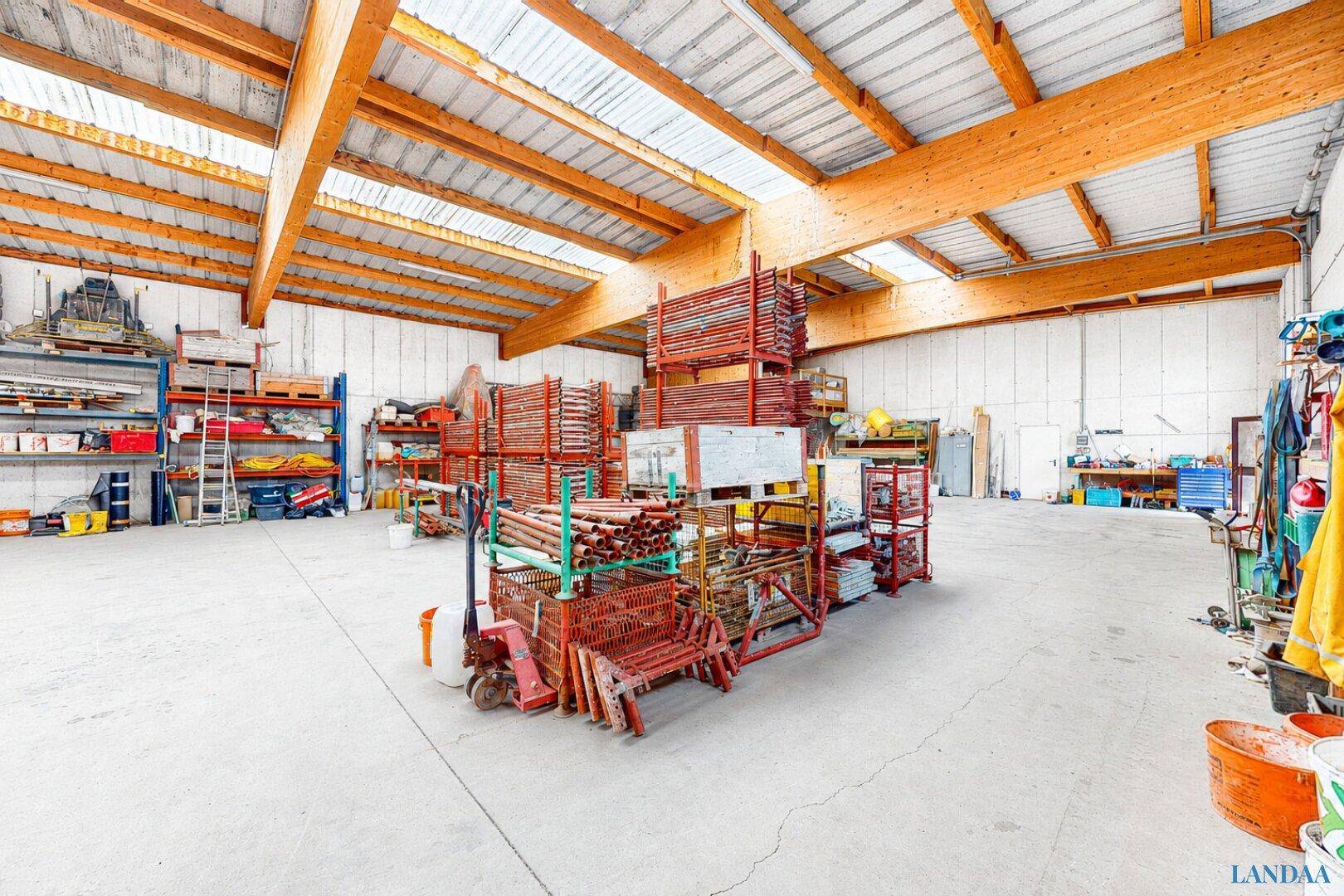 Lagerhalle gefüllt mit Baumaterialien und Geräten auf Regalen, mit Betonboden und sichtbaren Holzbalken.