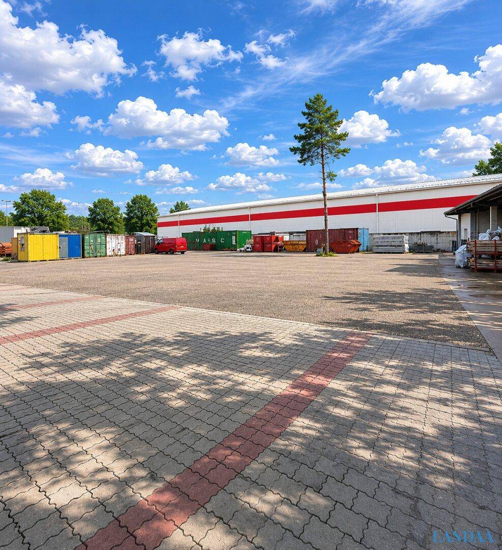 Großer gepflasterter Parkplatz mit roten Markierungen, Containern und einem Industriegebäude im Hintergrund.