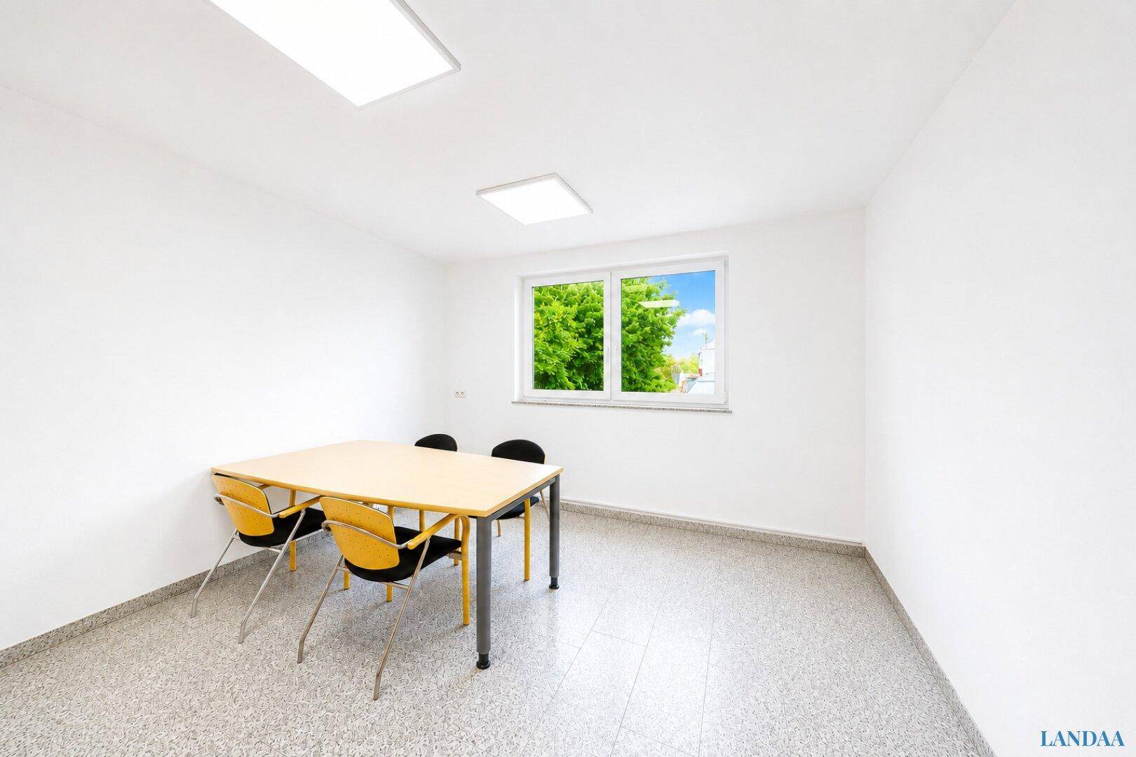 Kleiner Besprechungsraum oder Büro mit Tisch, Stühlen, weißen Wänden und hellem Terrazzoboden.