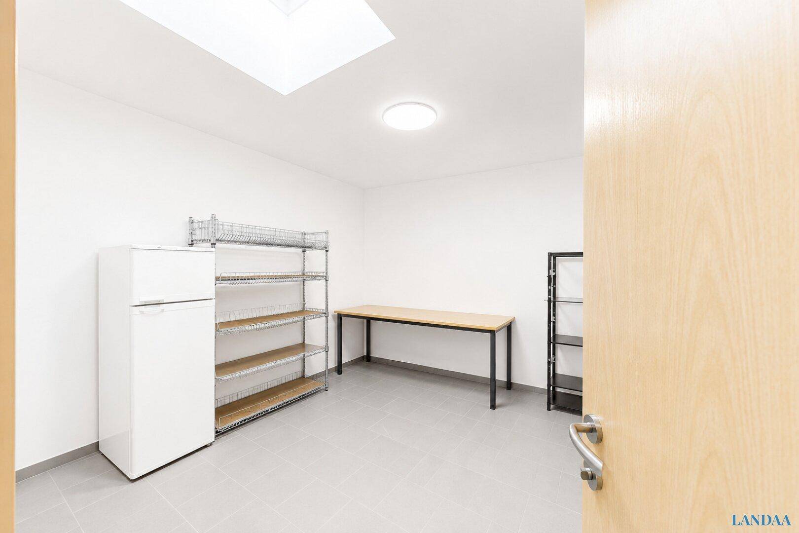 Abstellraum oder Speisekammer mit Kühlschrank, Metallregalen, Werkbank und hellem Fliesenboden.